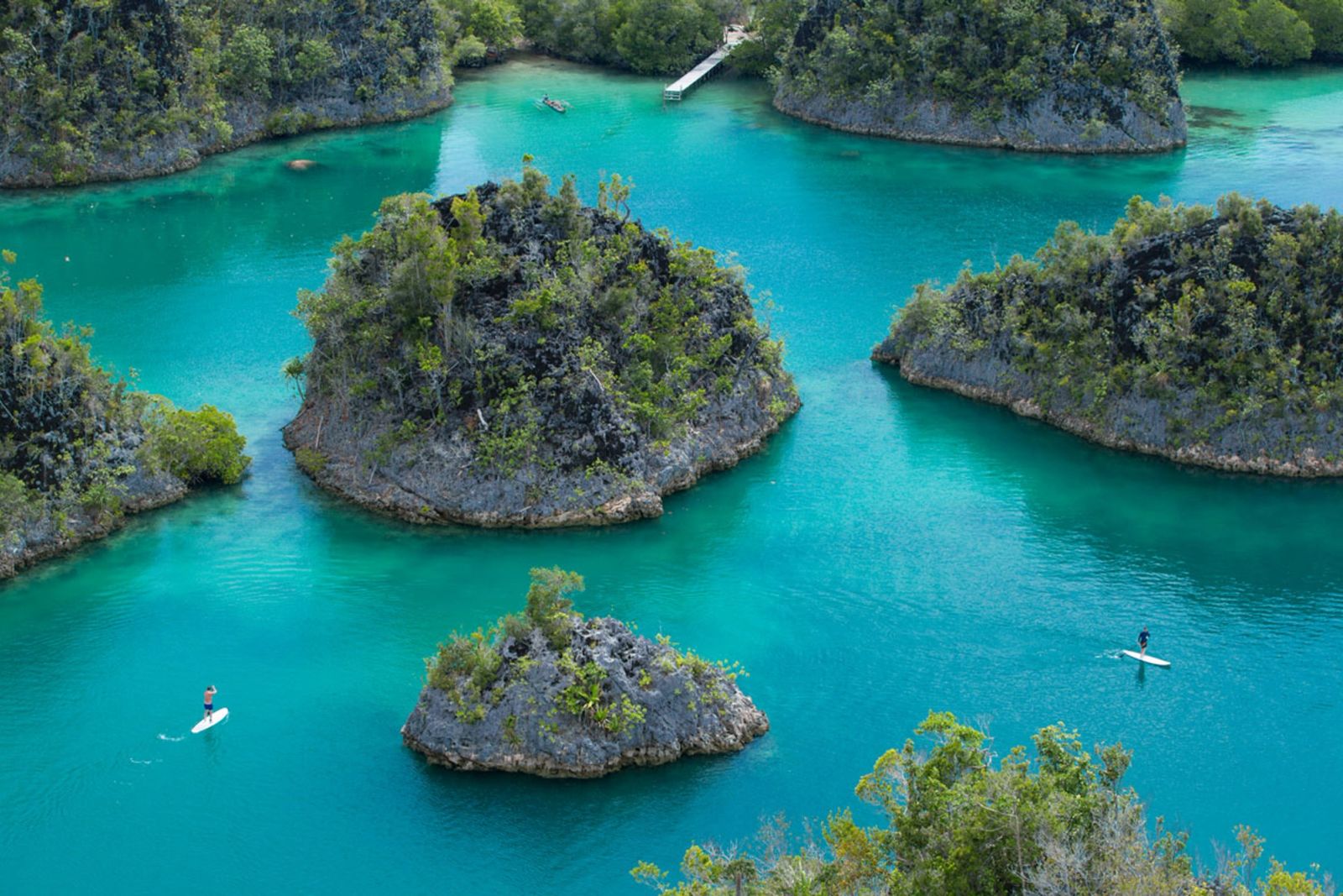 Paddleboarders crossing the turquoise lagoons among the karst islets of Piaynemo