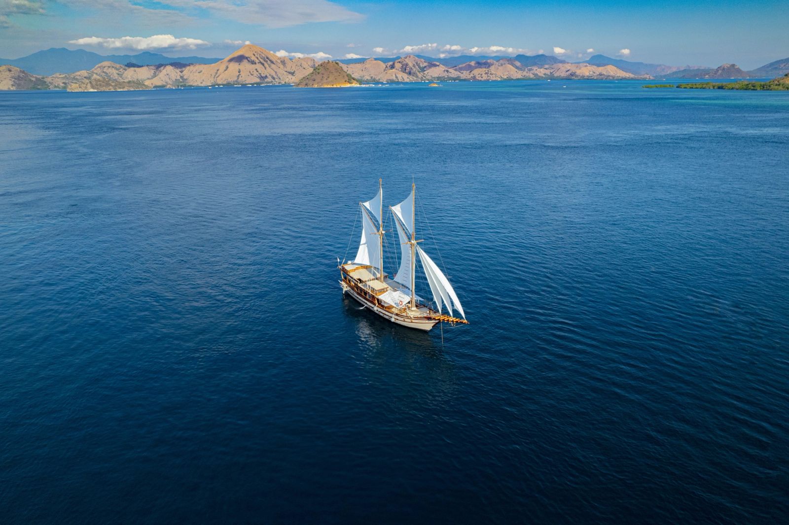 Nataraja sailing across open blue water below distant hills, from the air.