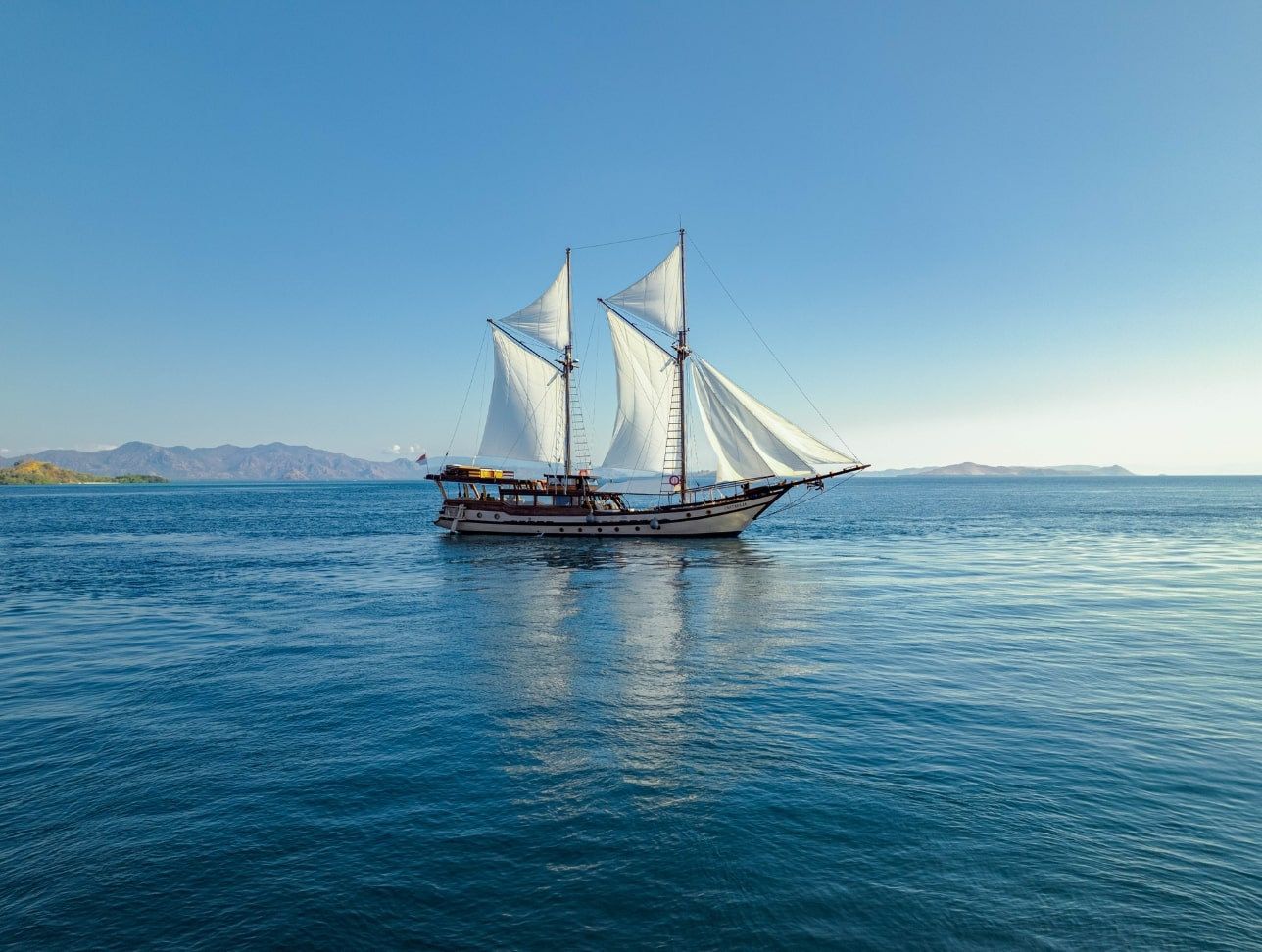 Nataraja under full sail on calm water with islands on the horizon.