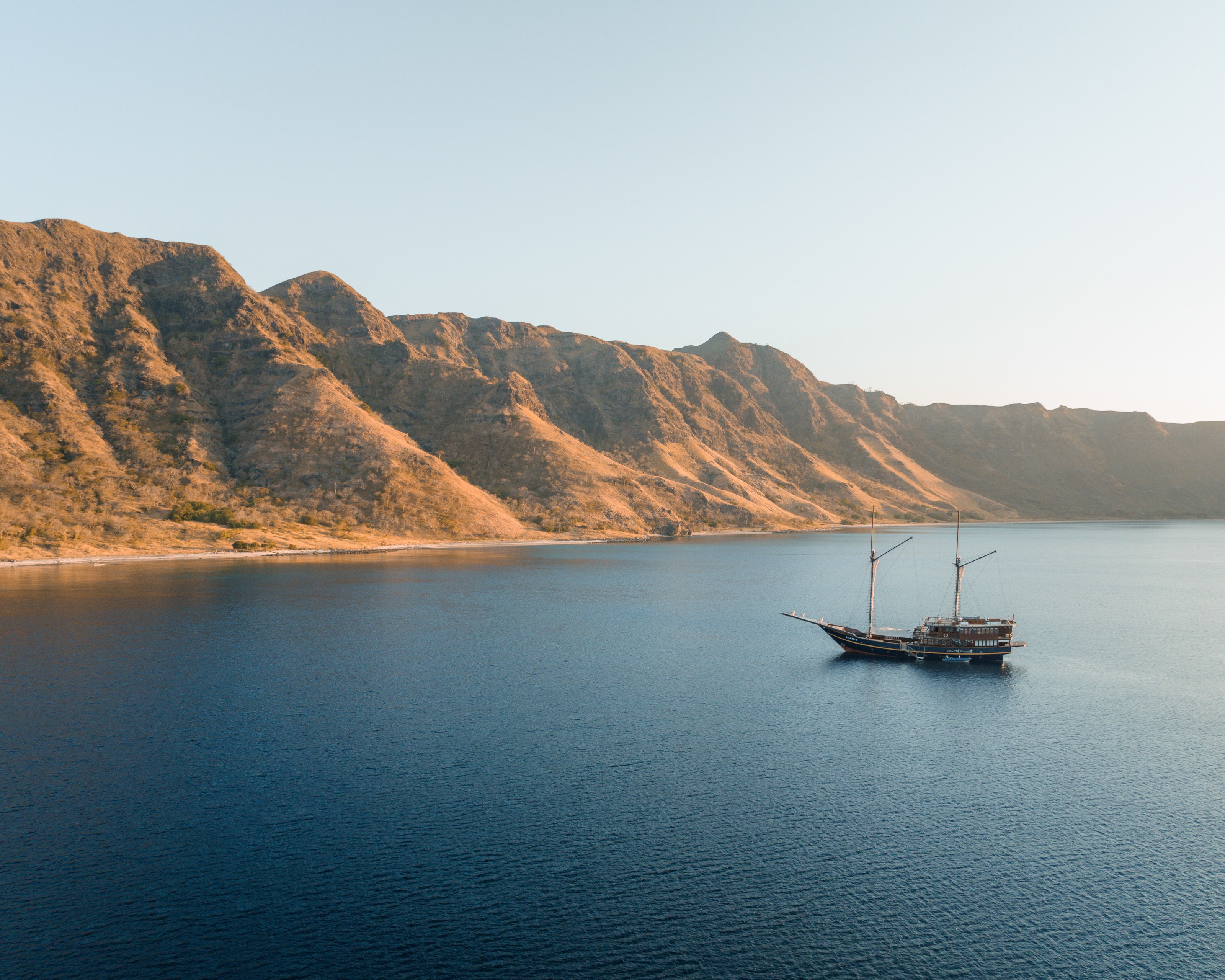 Celestia at anchor beneath dry rugged hills.
