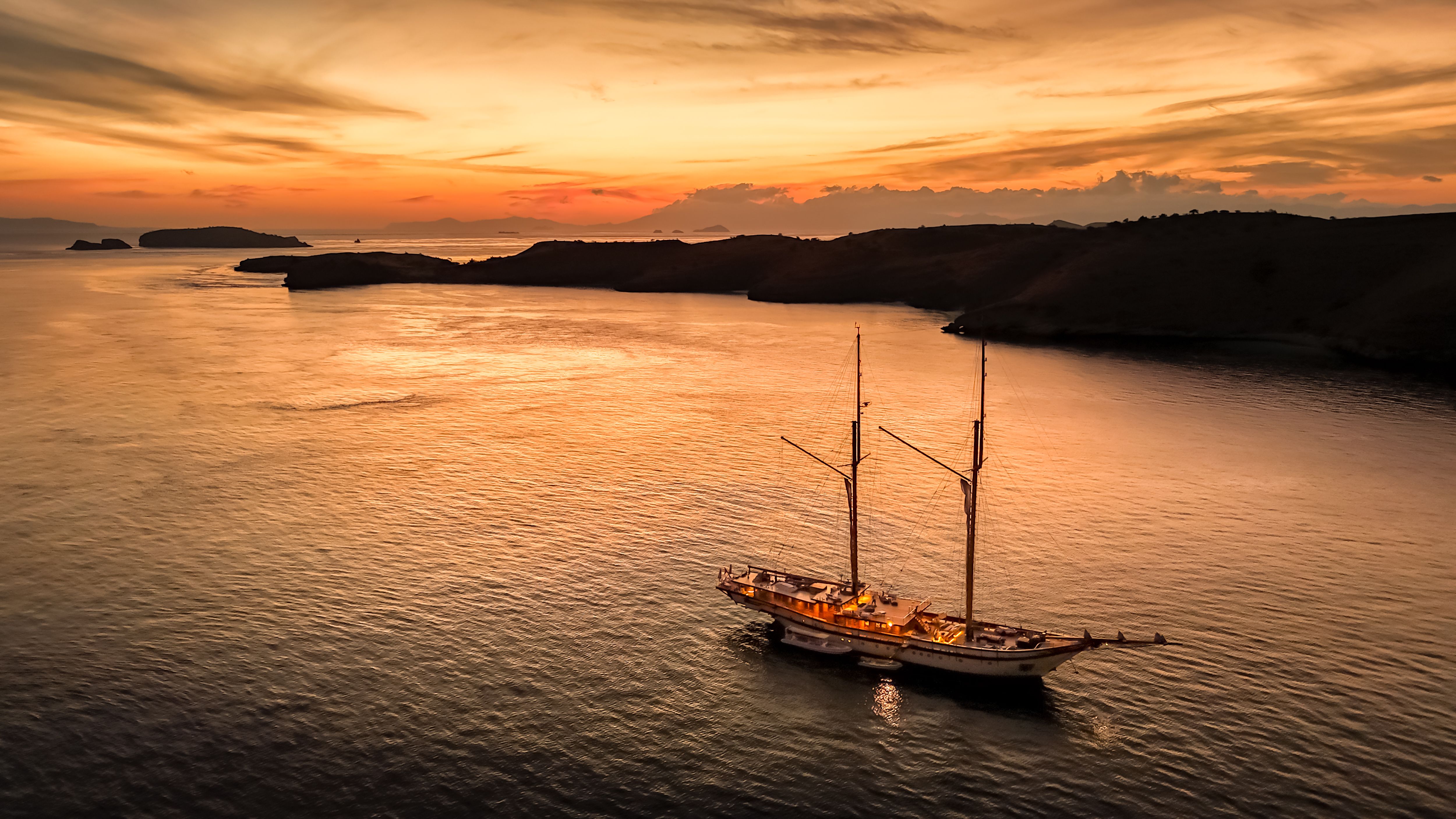 Aerial view of a phinisi anchored alone in a calm bay in Komodo as the sun sets.