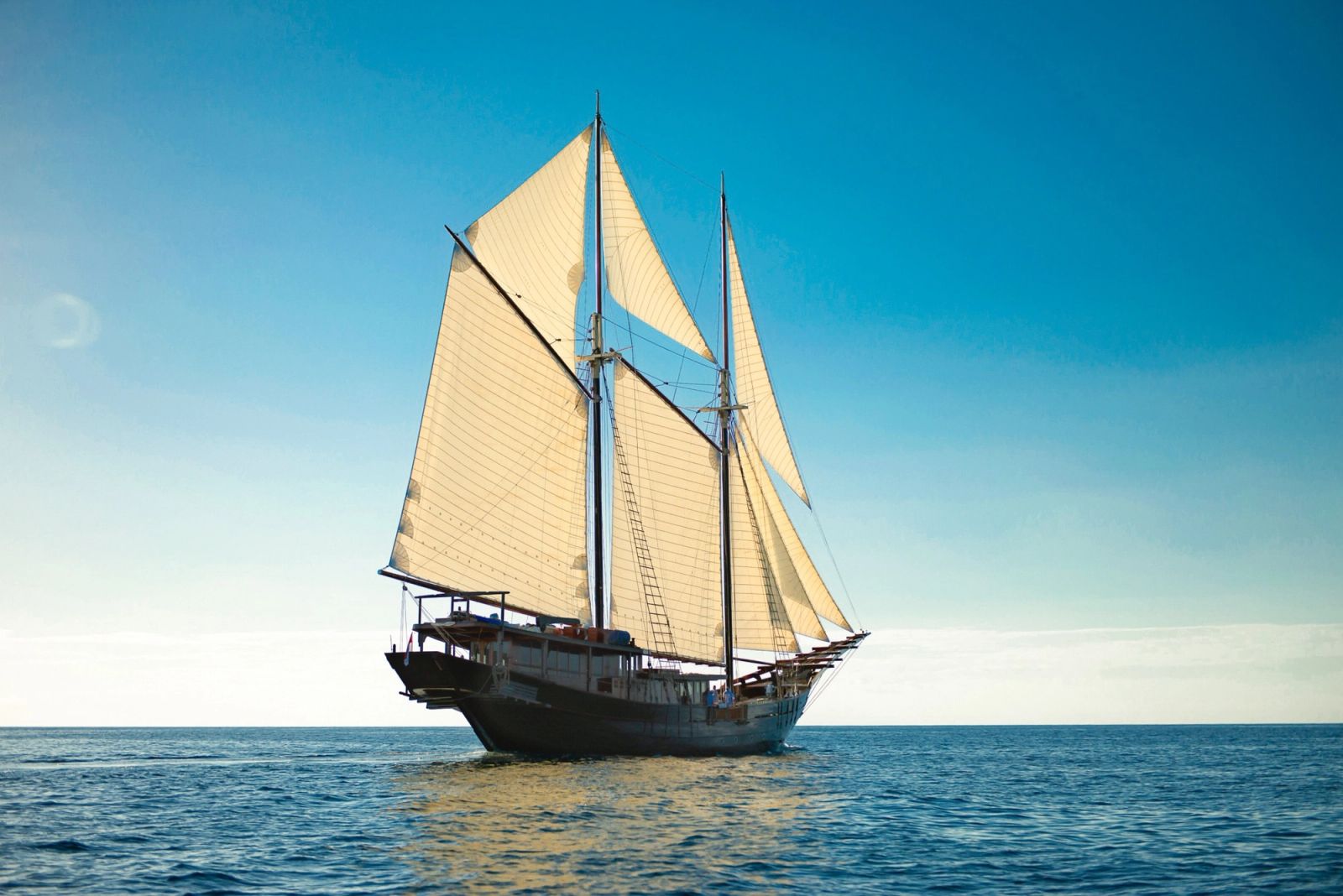 A phinisi under sail, the way a Bali charter carries on east.
