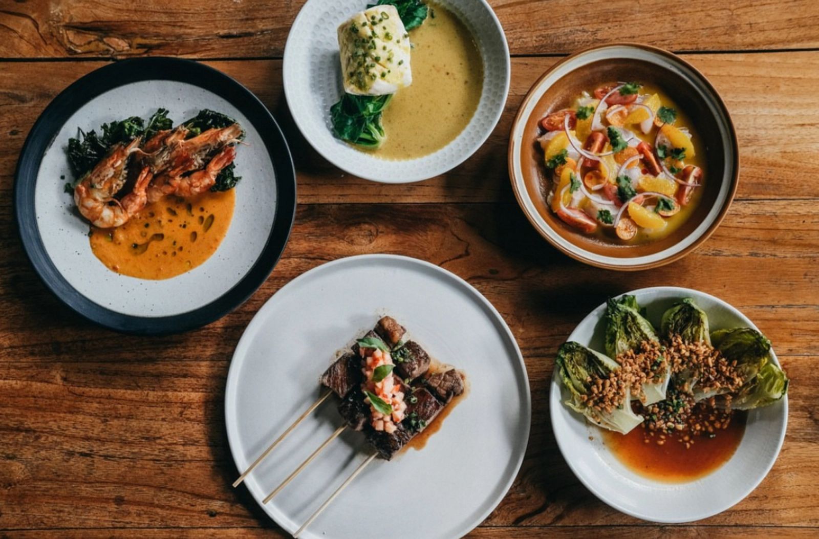 An overhead view of several plated dishes on a wooden table.