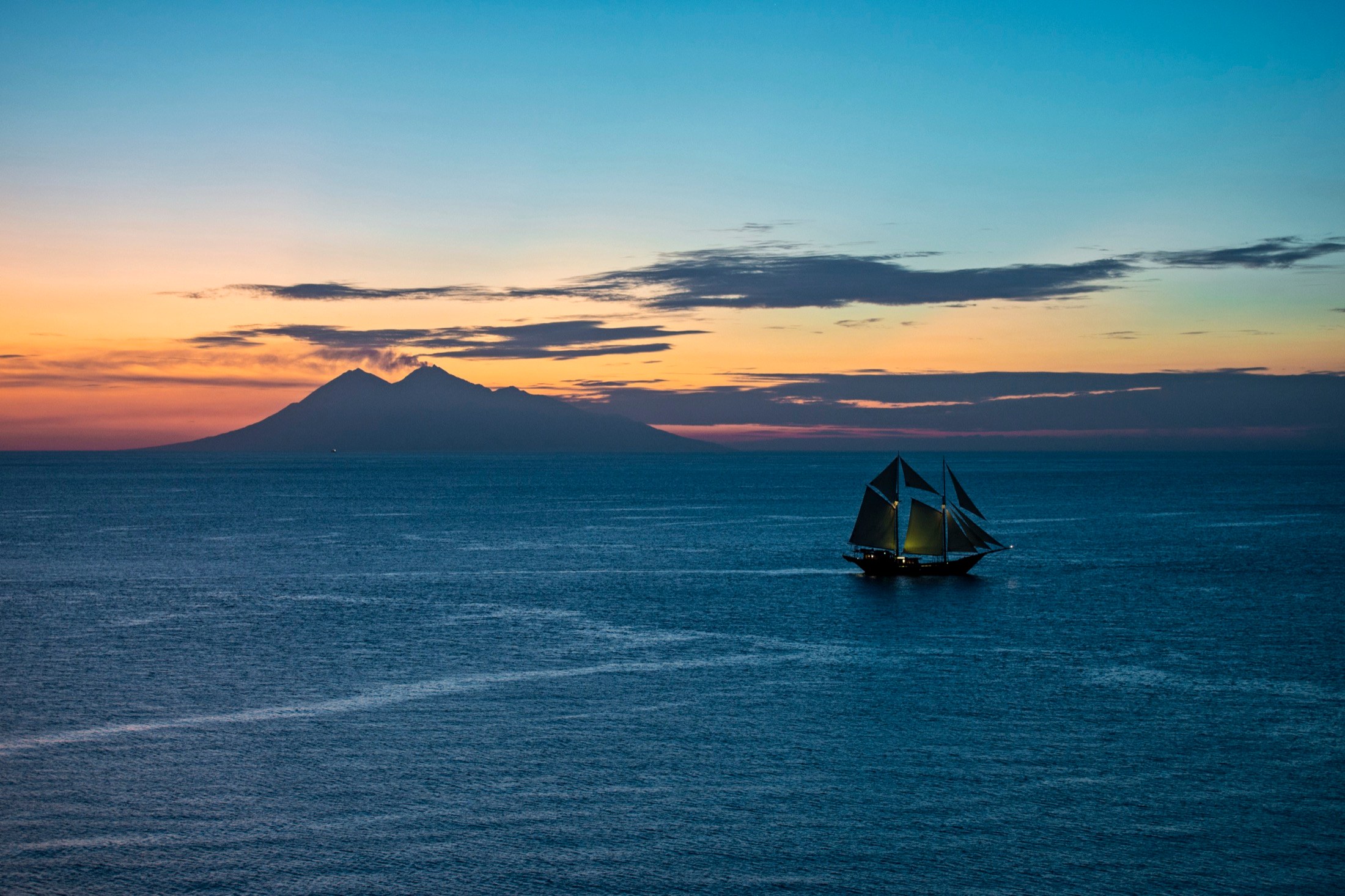 A phinisi silhouette at dusk off the Komodo hills