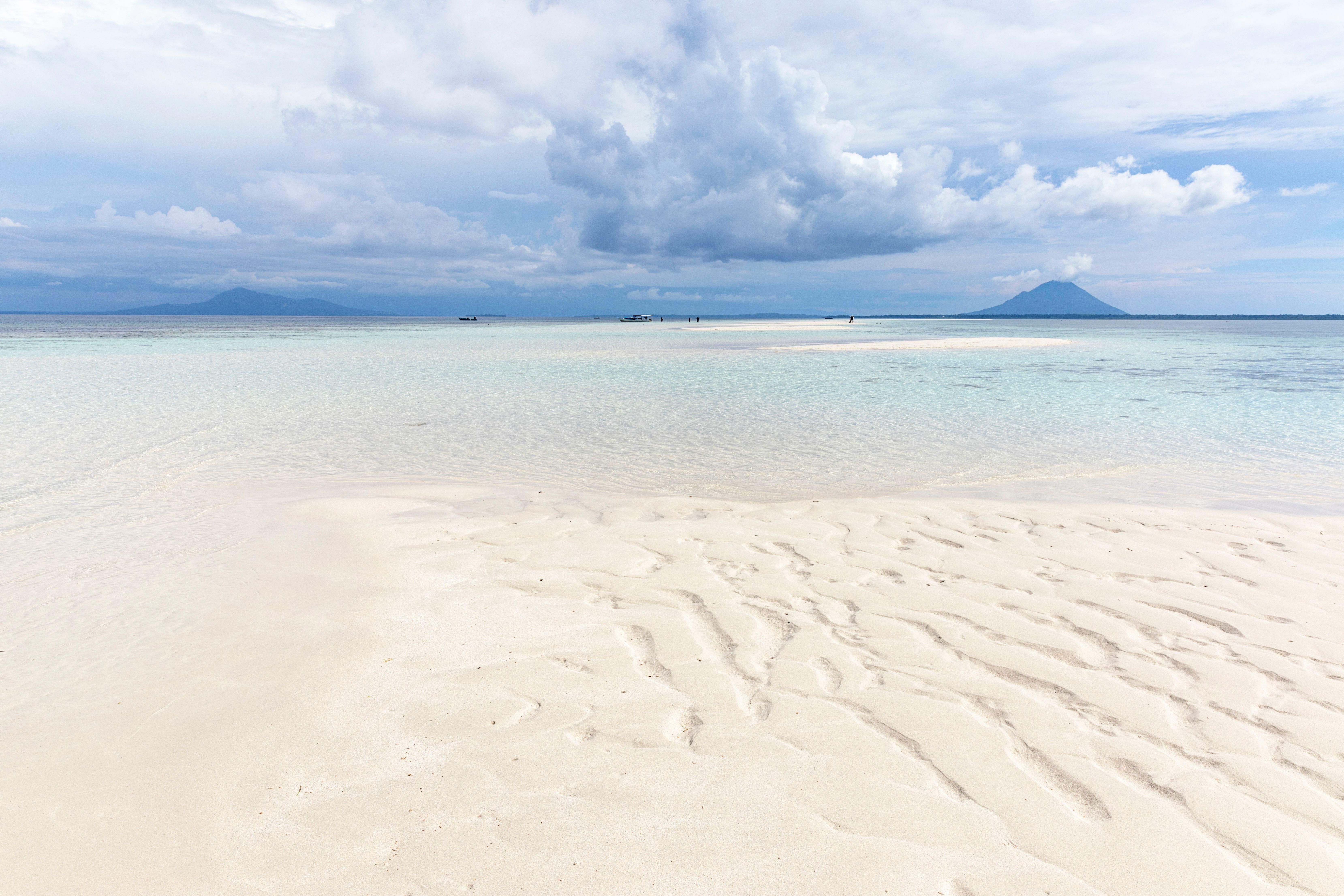 Rippled white sand and shallow water with a distant volcano