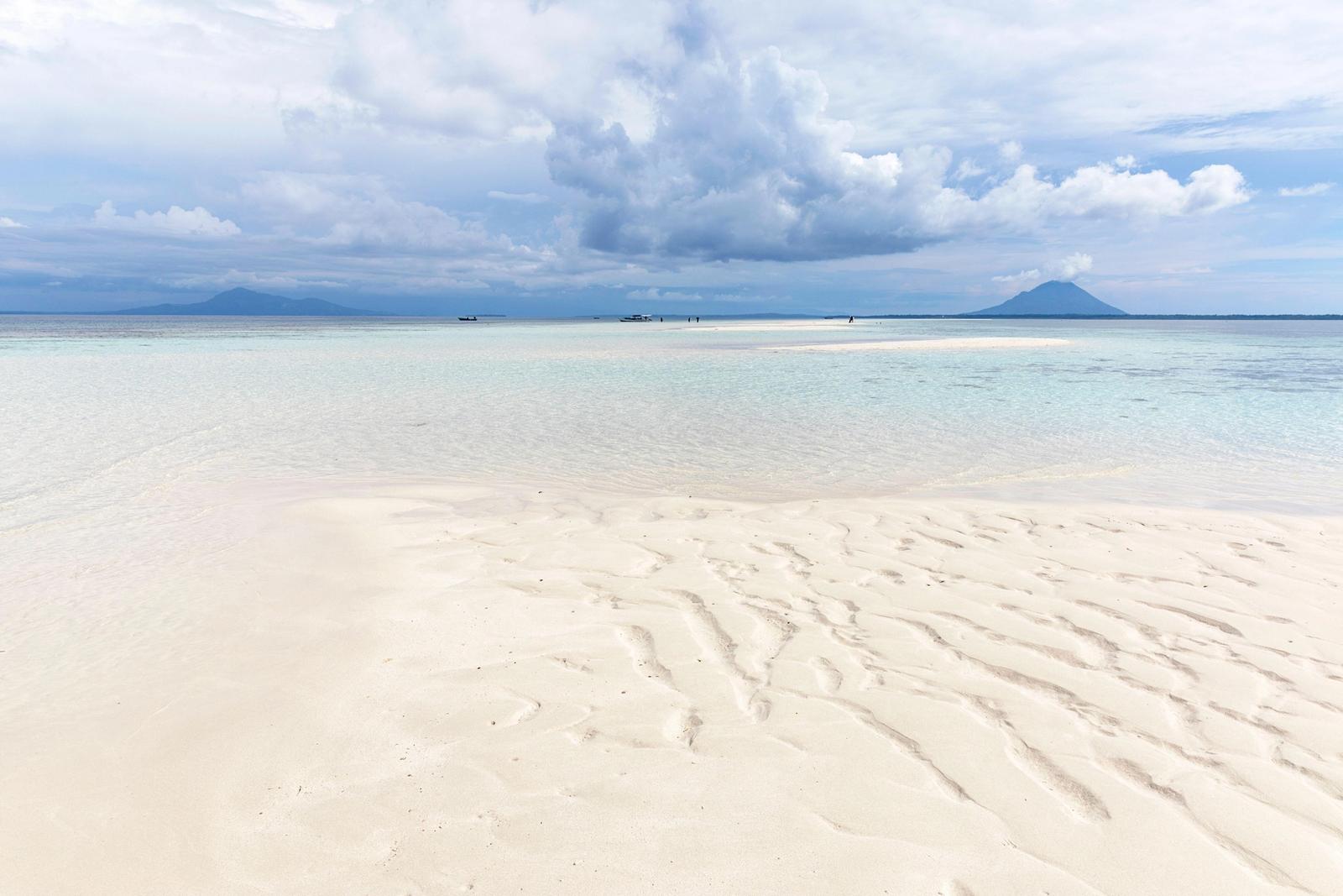 Rippled white sand and shallow water with a distant volcano