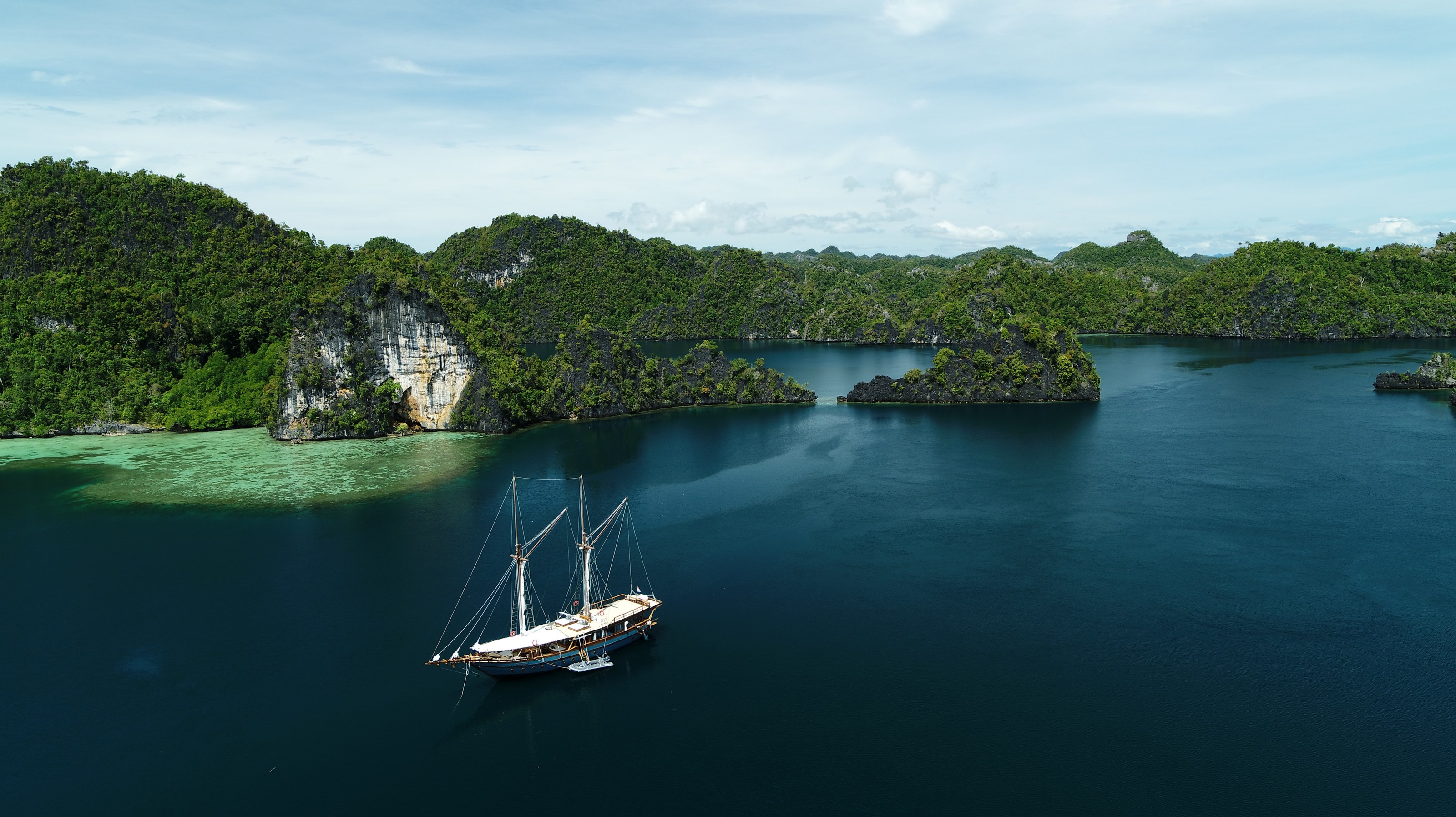 A distant aerial view of Dewata at anchor among forested islands.