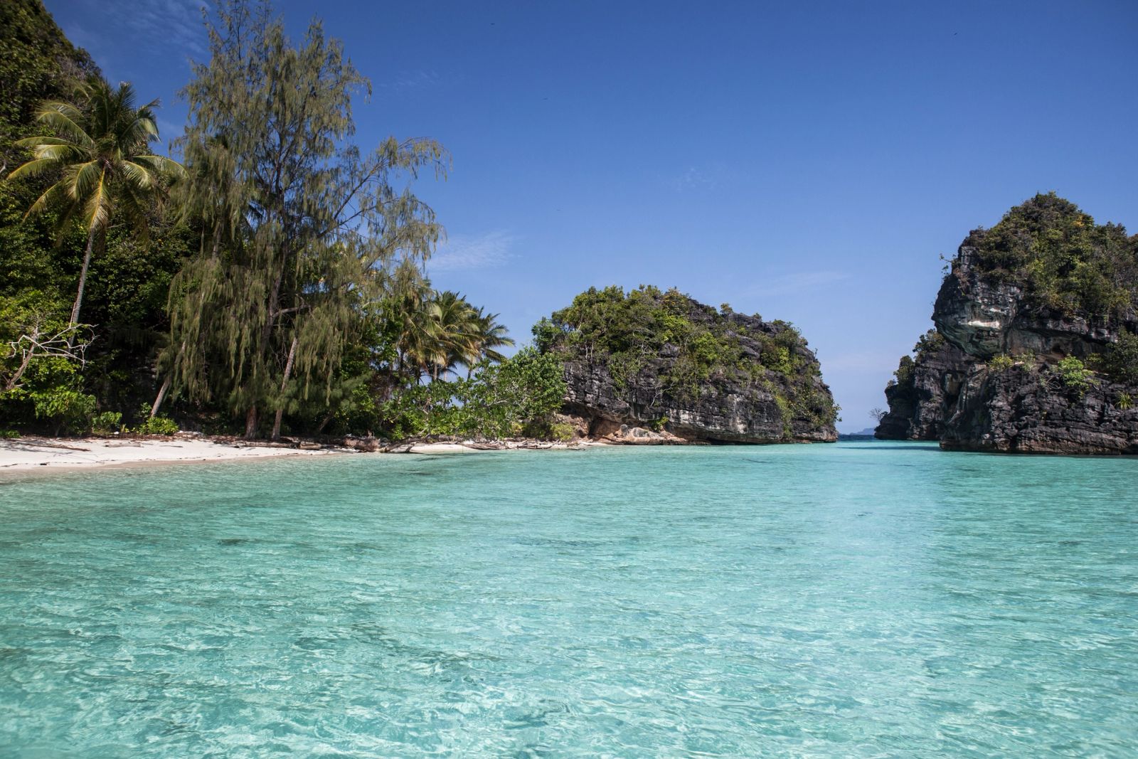 A small white beach and clear shallows below forested limestone near Misool