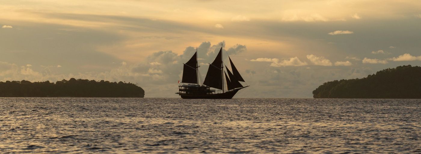Dunia Baru's silhouette under sail at dusk in the Spice Islands