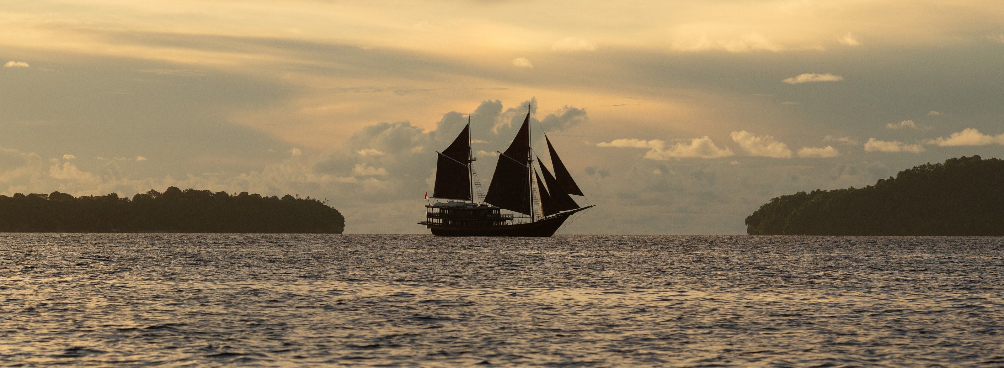 Dunia Baru's silhouette under sail at dusk in the Spice Islands