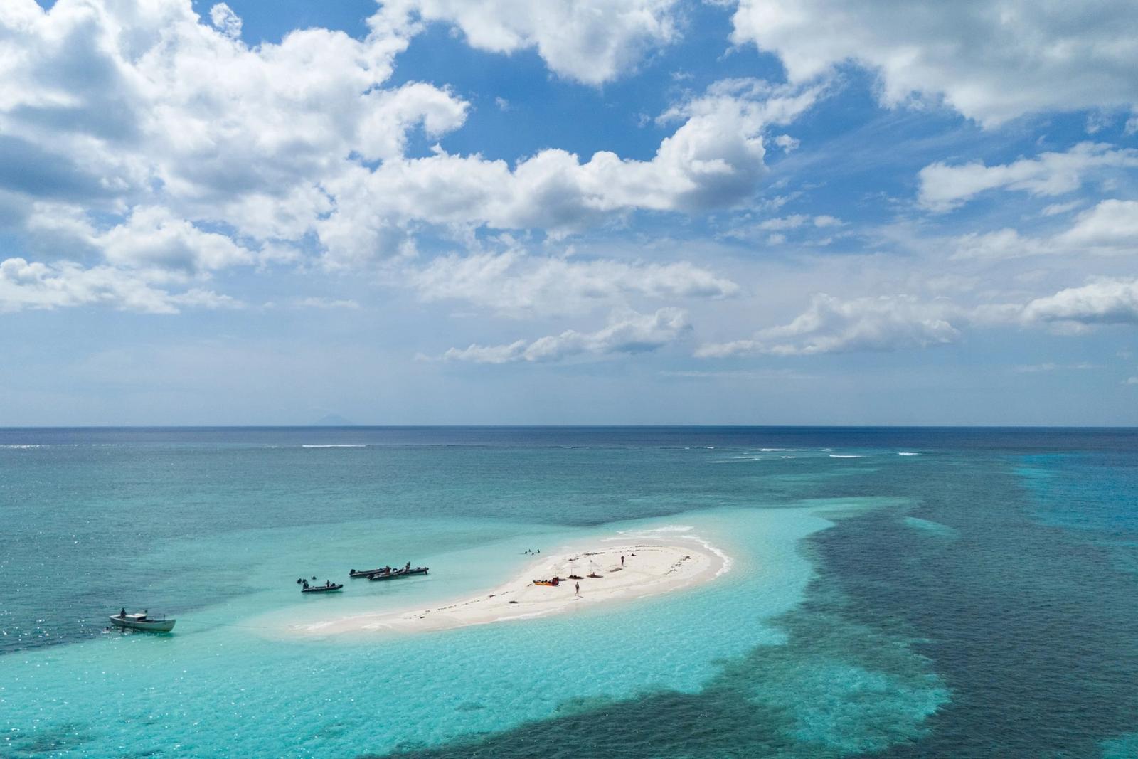 A white sandbar ringed by reef with boats nearby, from the air