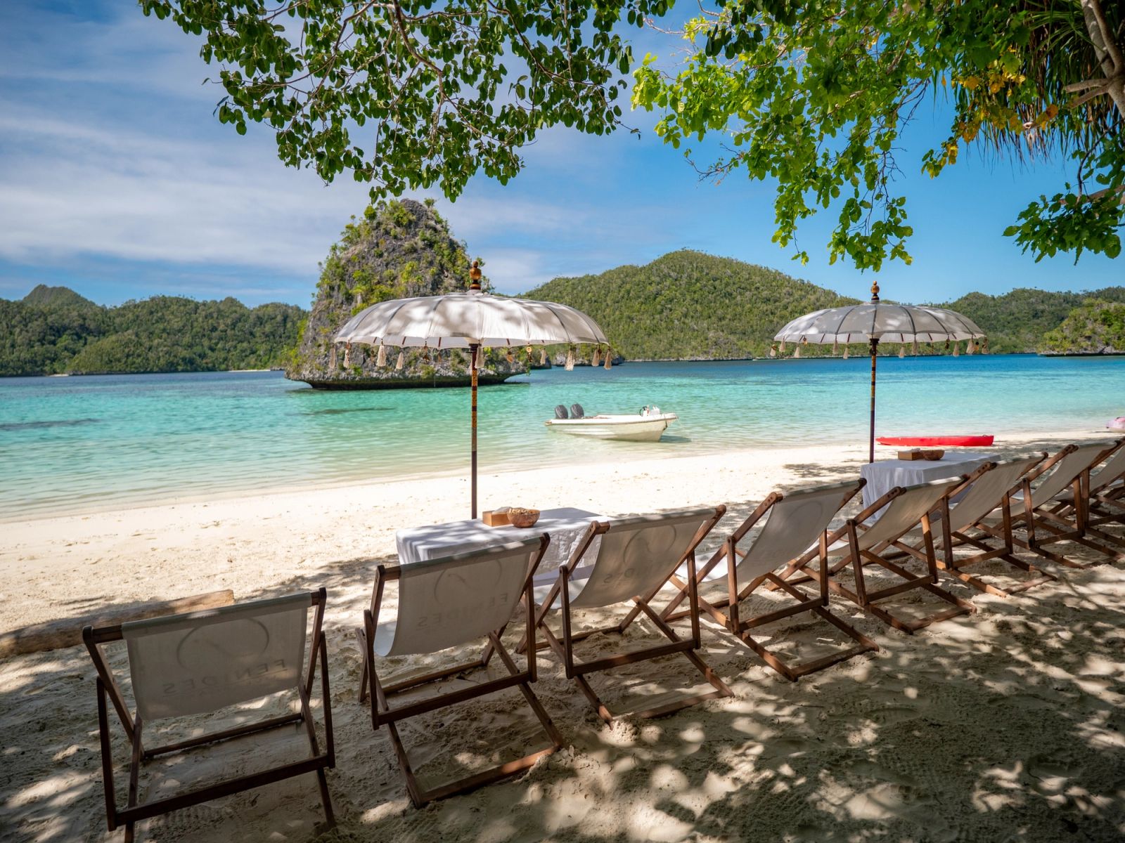 Beach chairs and parasols set out on a white beach below karst islands
