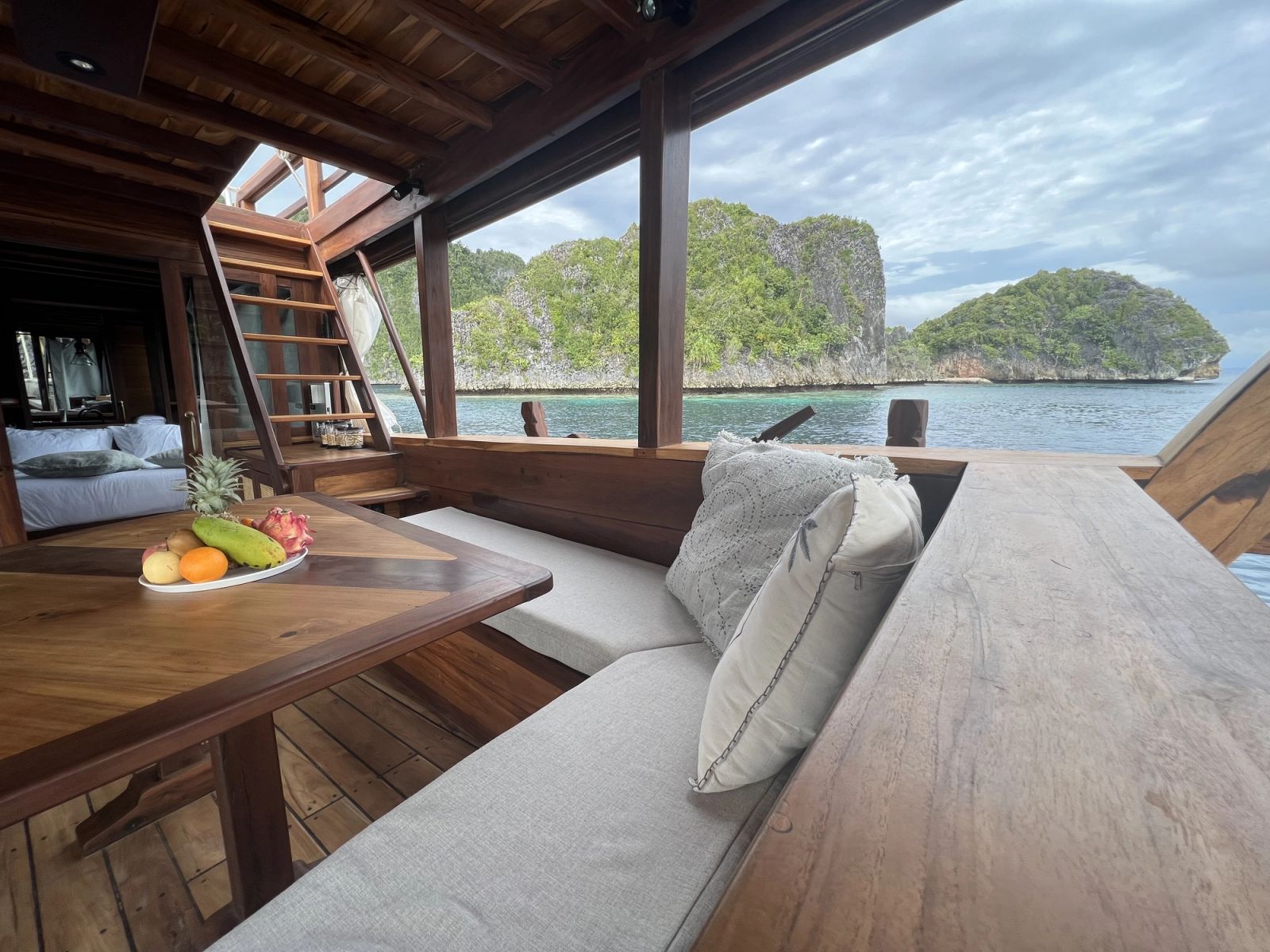 The chill deck on Dewata with a wooden table, a fruit bowl and a cushioned bench.