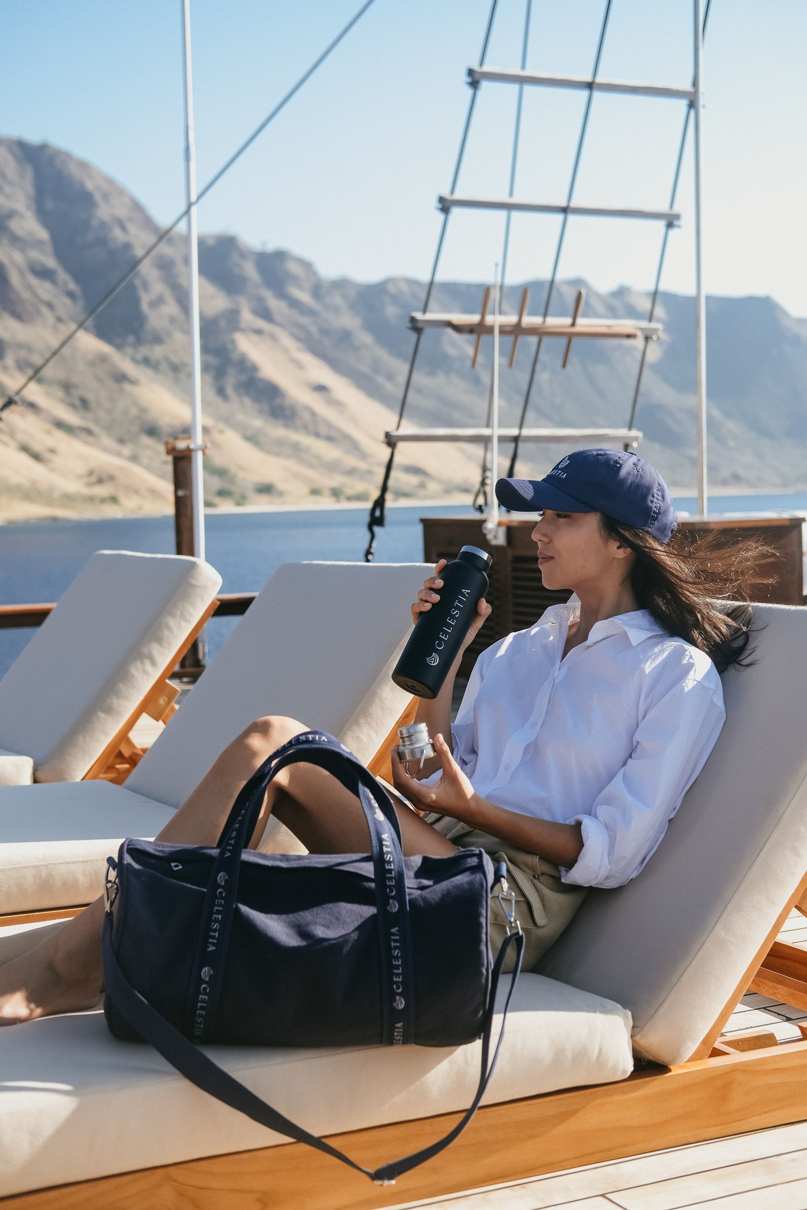 A woman with binoculars on a sunbed with a navy Celestia bag beside her.