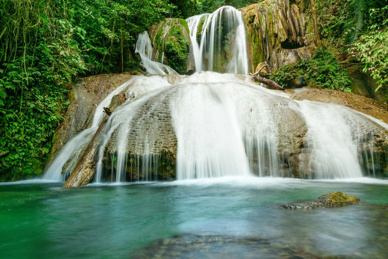 A jungle waterfall spilling into a green pool, one of North Sulawesi's pleasures above the surface.