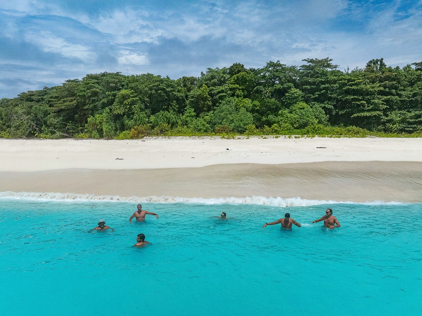 Guests swimming in turquoise water beside a white sand beach.