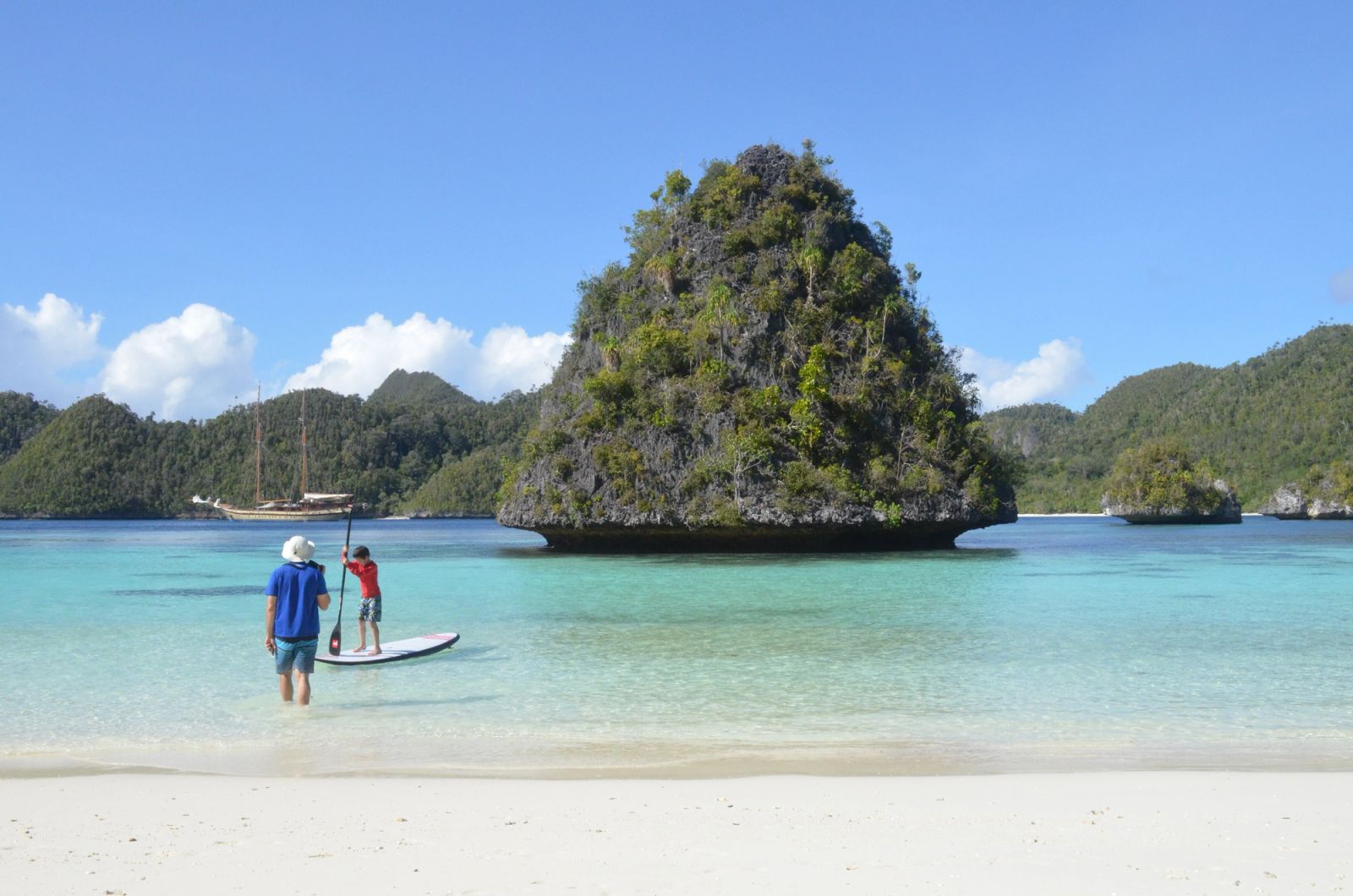 Guests carrying a paddleboard into the shallows below a karst island