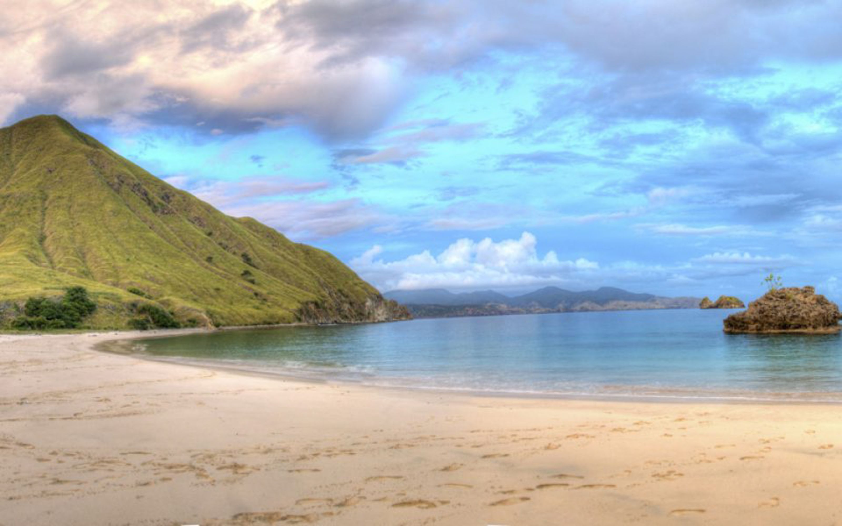 A curving beach below a green hill at Gili Lawa