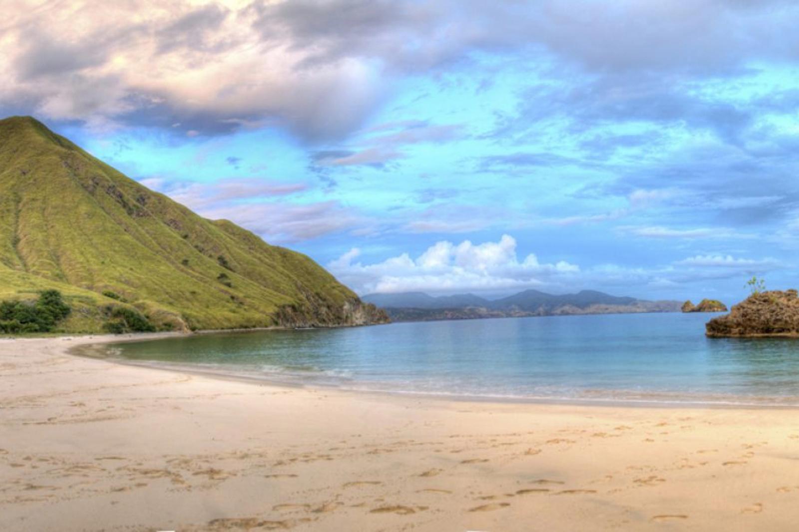 A curving beach below a green hill at Gili Lawa