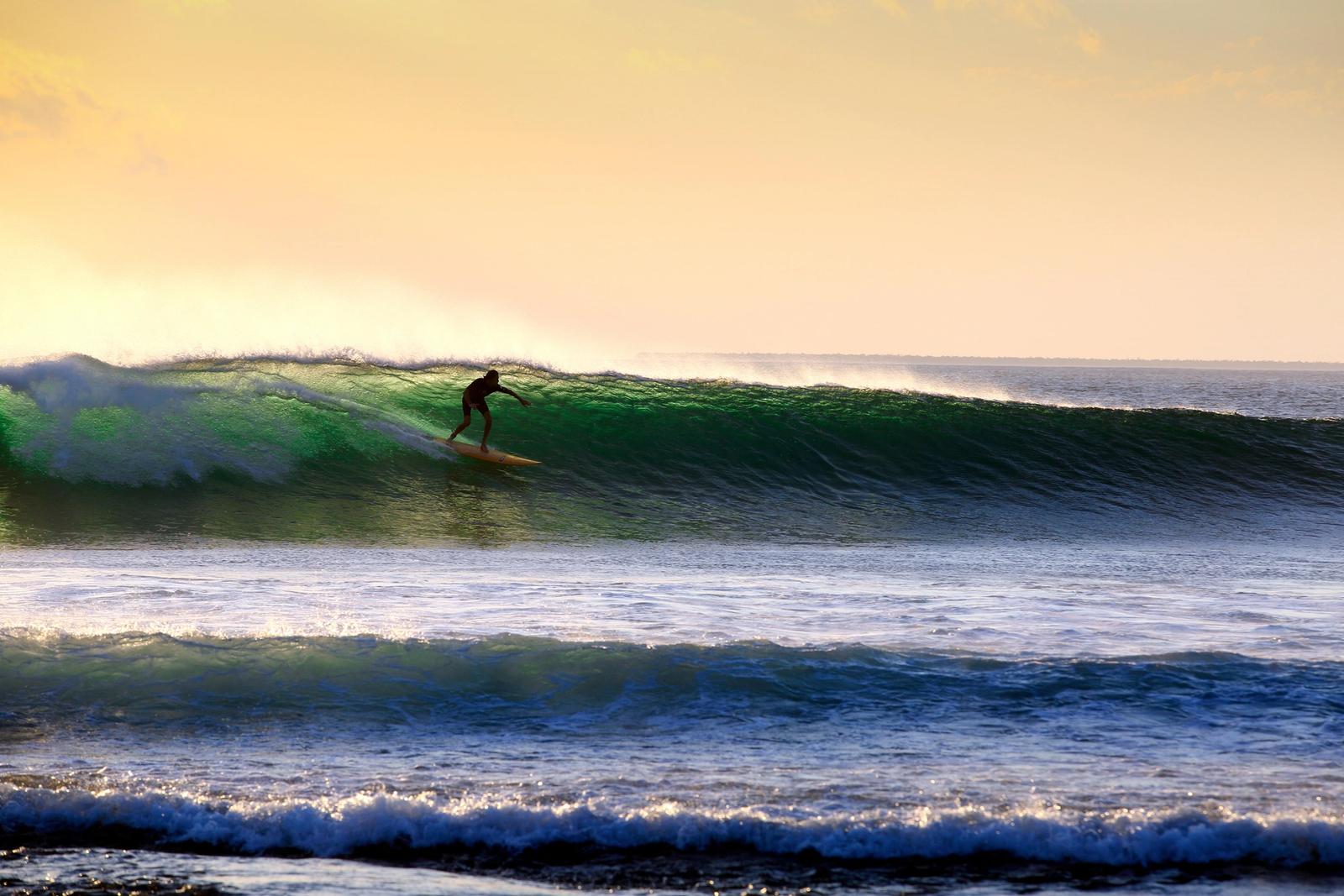 A lone surfer riding a wave in golden evening light