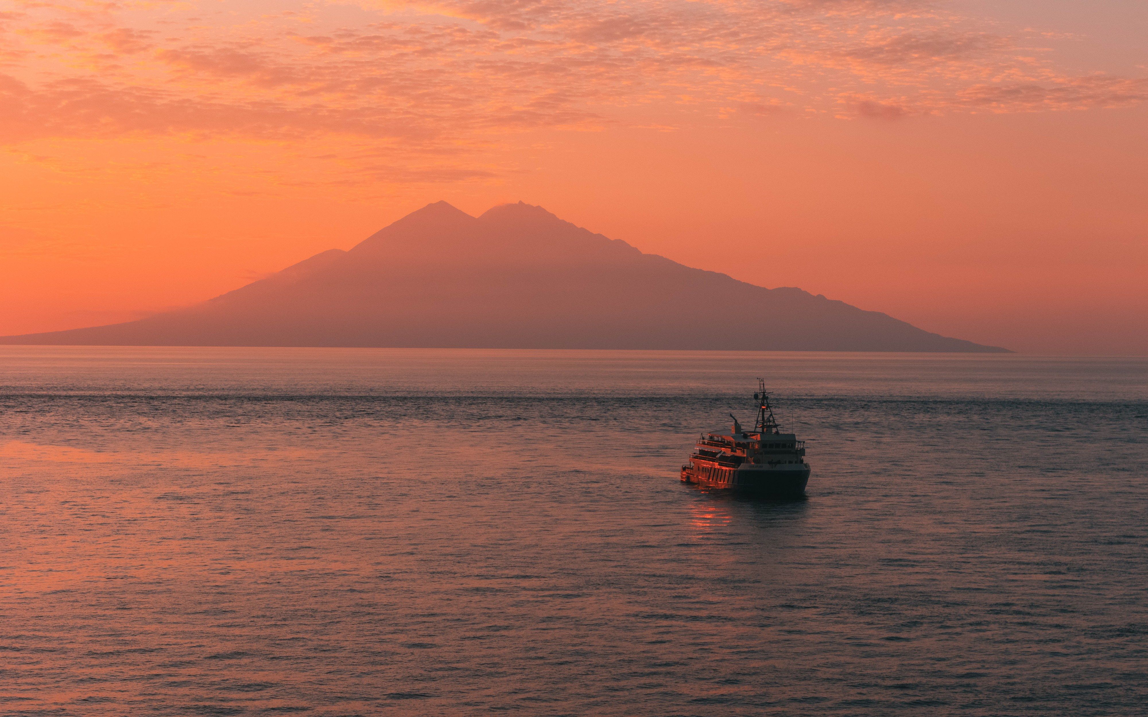 Kudanil Explorer under way on calm water below a volcano at sunset