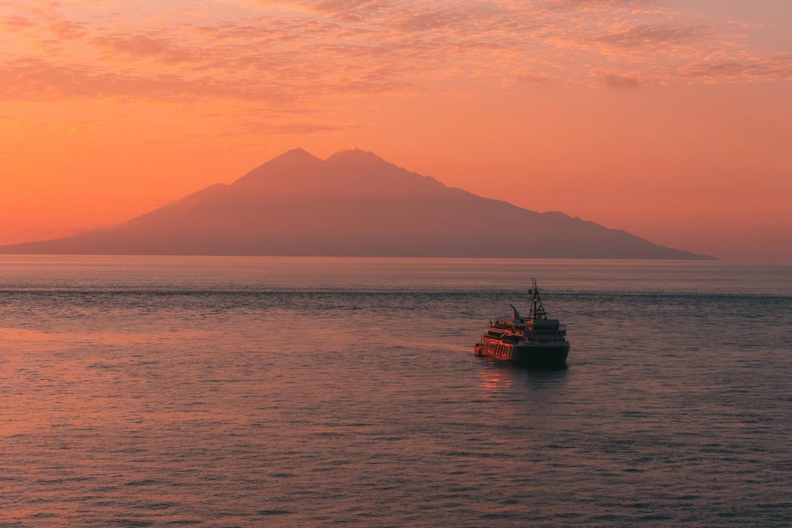 Kudanil Explorer under way on calm water below a volcano at sunset