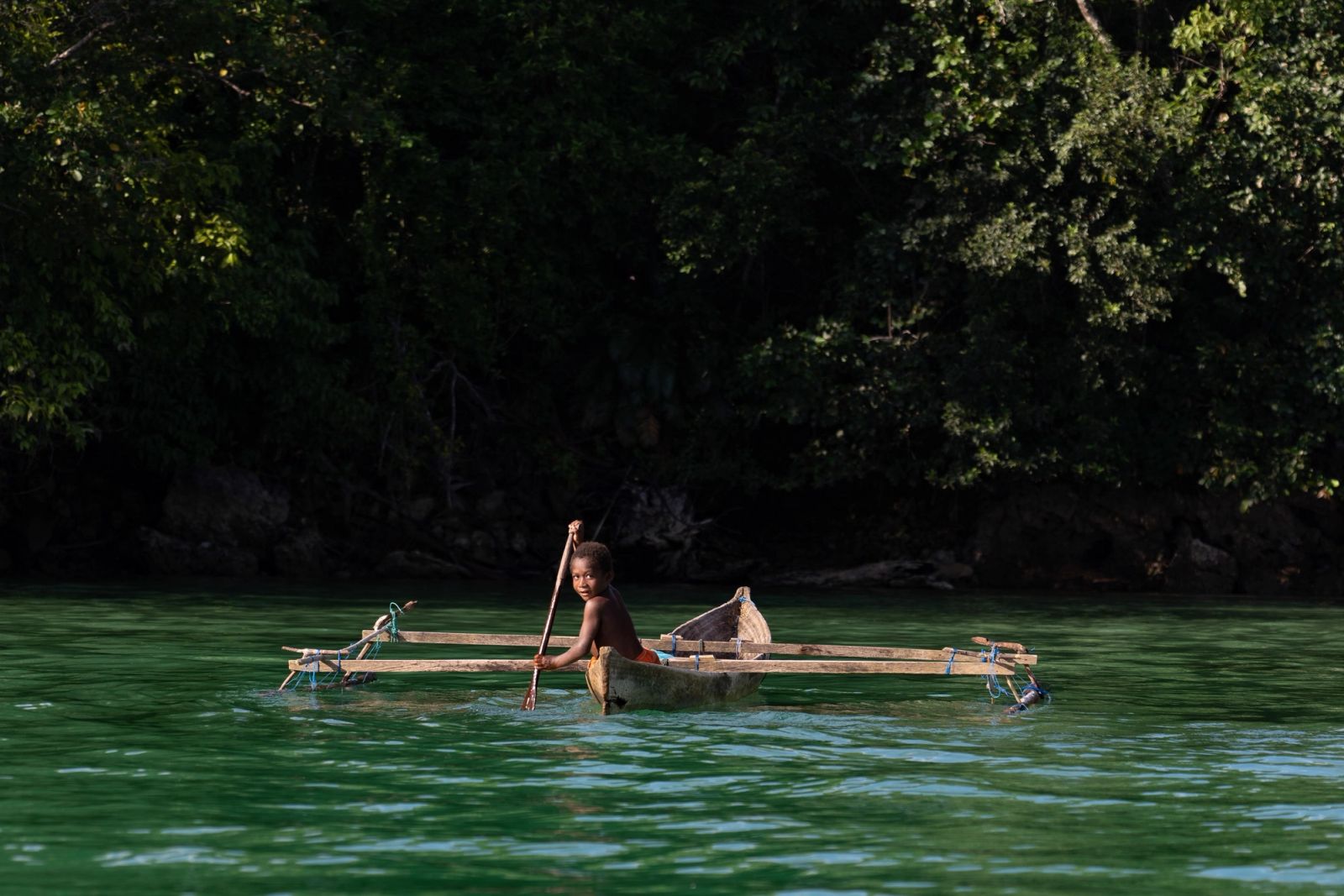 A paddler on a still, jungle-fringed creek, the quiet way into Triton Bay.