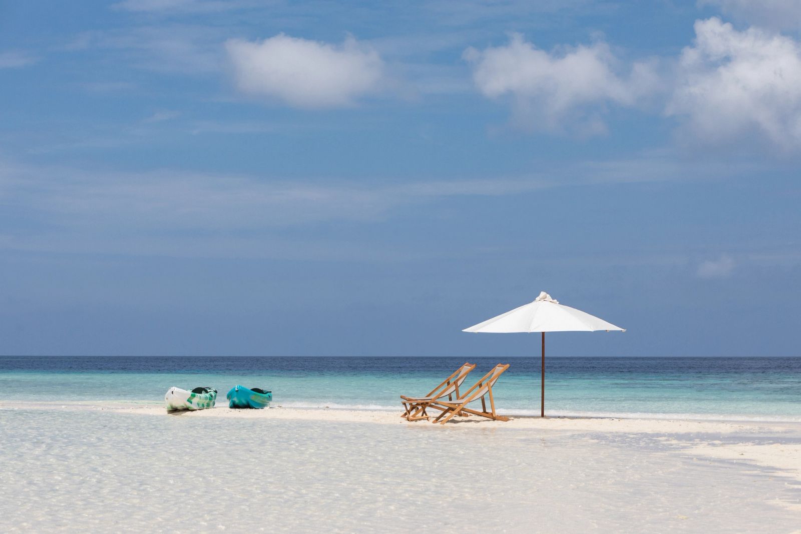 A parasol, deck chairs and kayaks set out on a white sandbar
