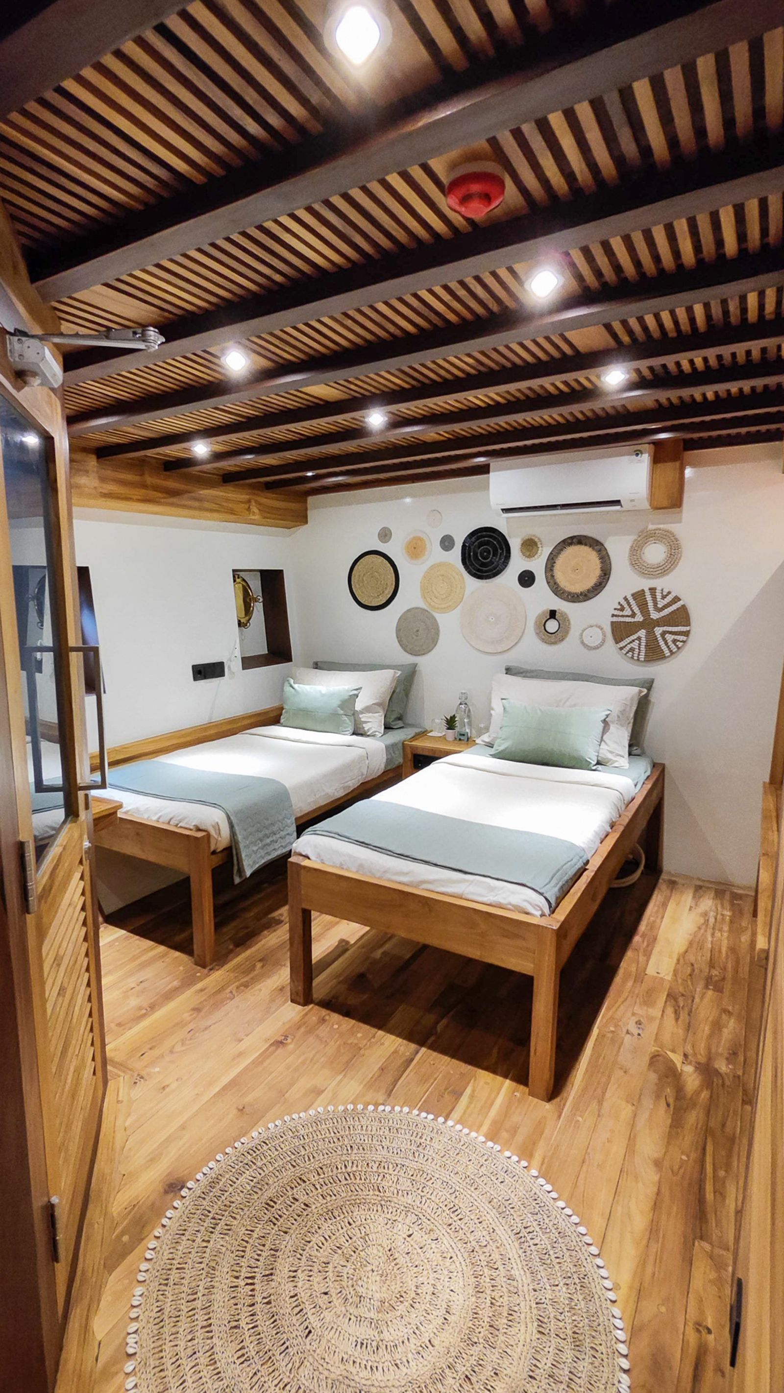 A twin cabin on Siloina with two beds and a round rug on the teak floor.