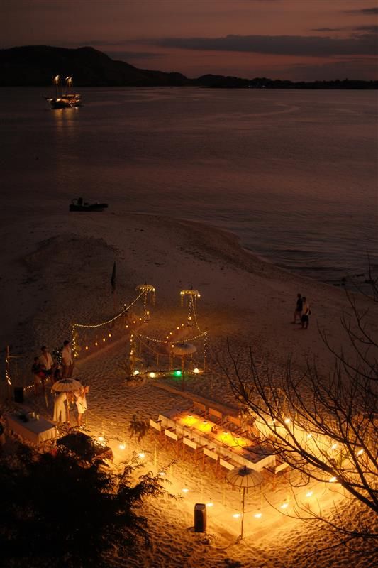 A dinner table on the sand lit by lanterns at night