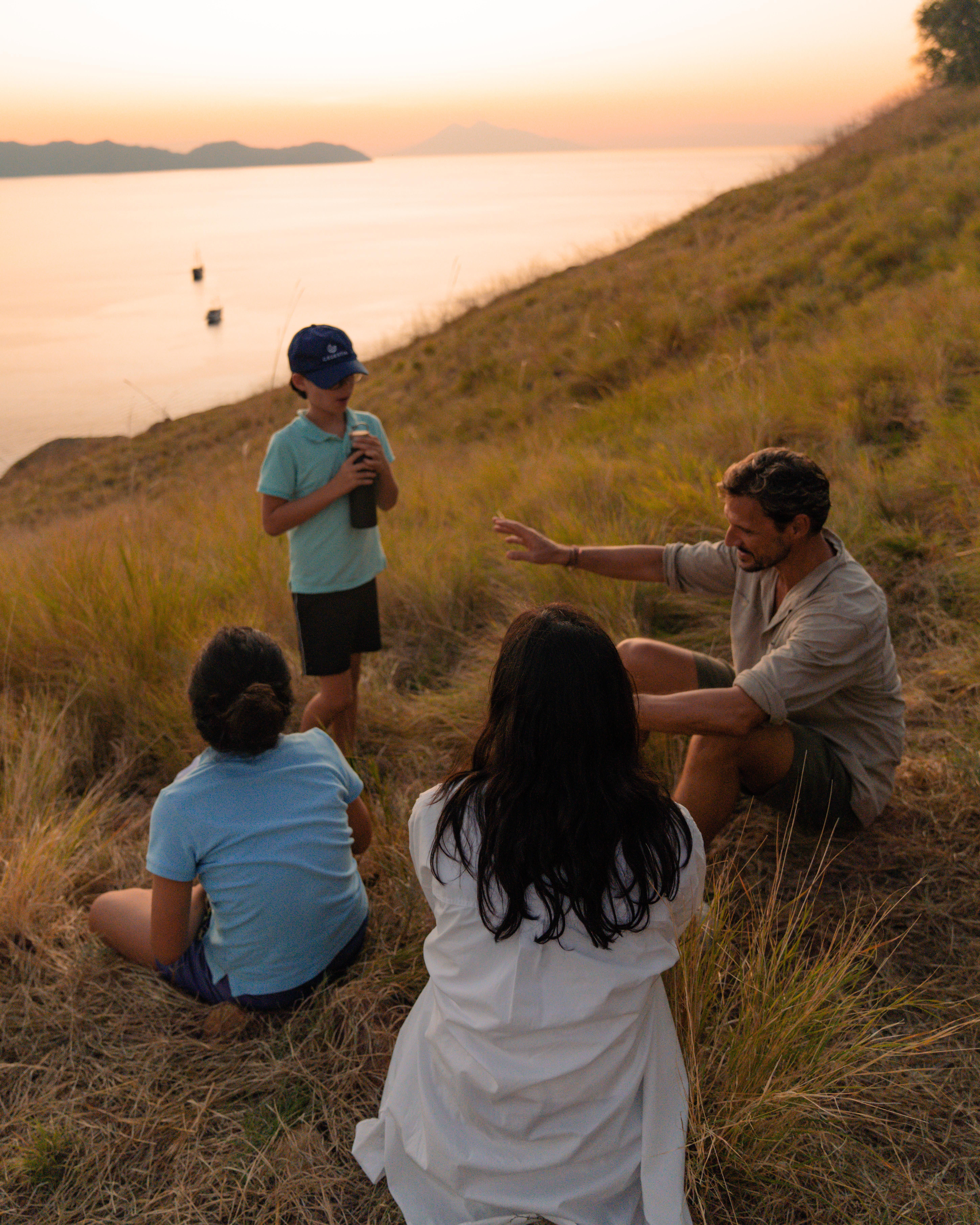 A family resting on a grassy Komodo hillside at golden hour