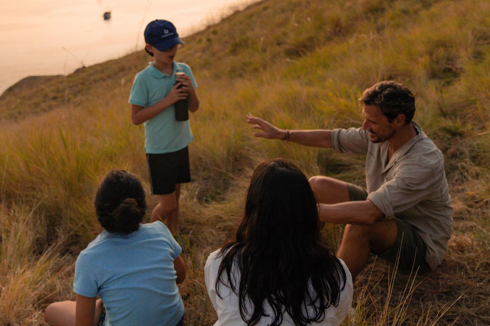 A family resting on a grassy Komodo hillside at golden hour
