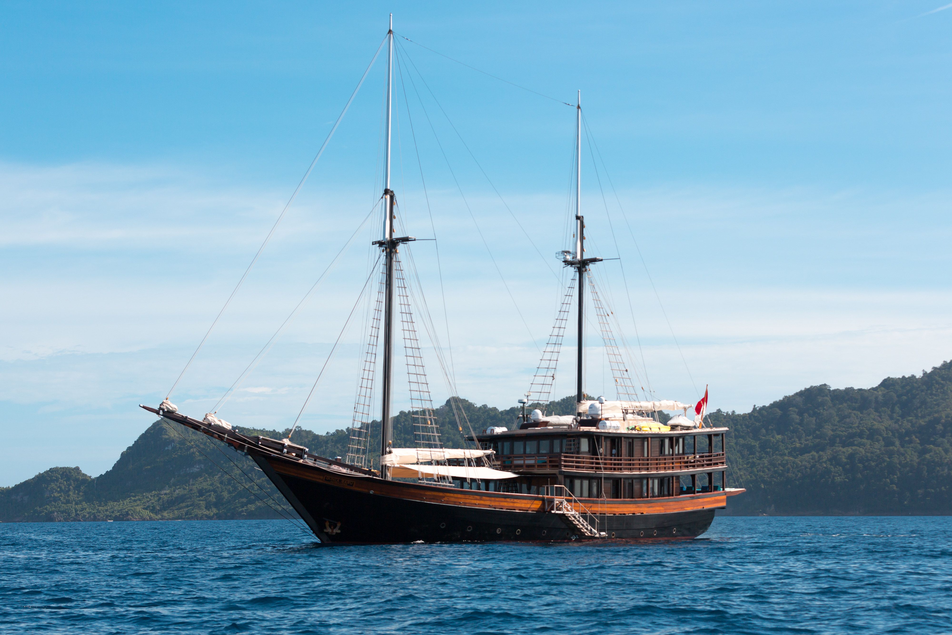 The phinisi Dunia Baru at anchor with forested hills behind