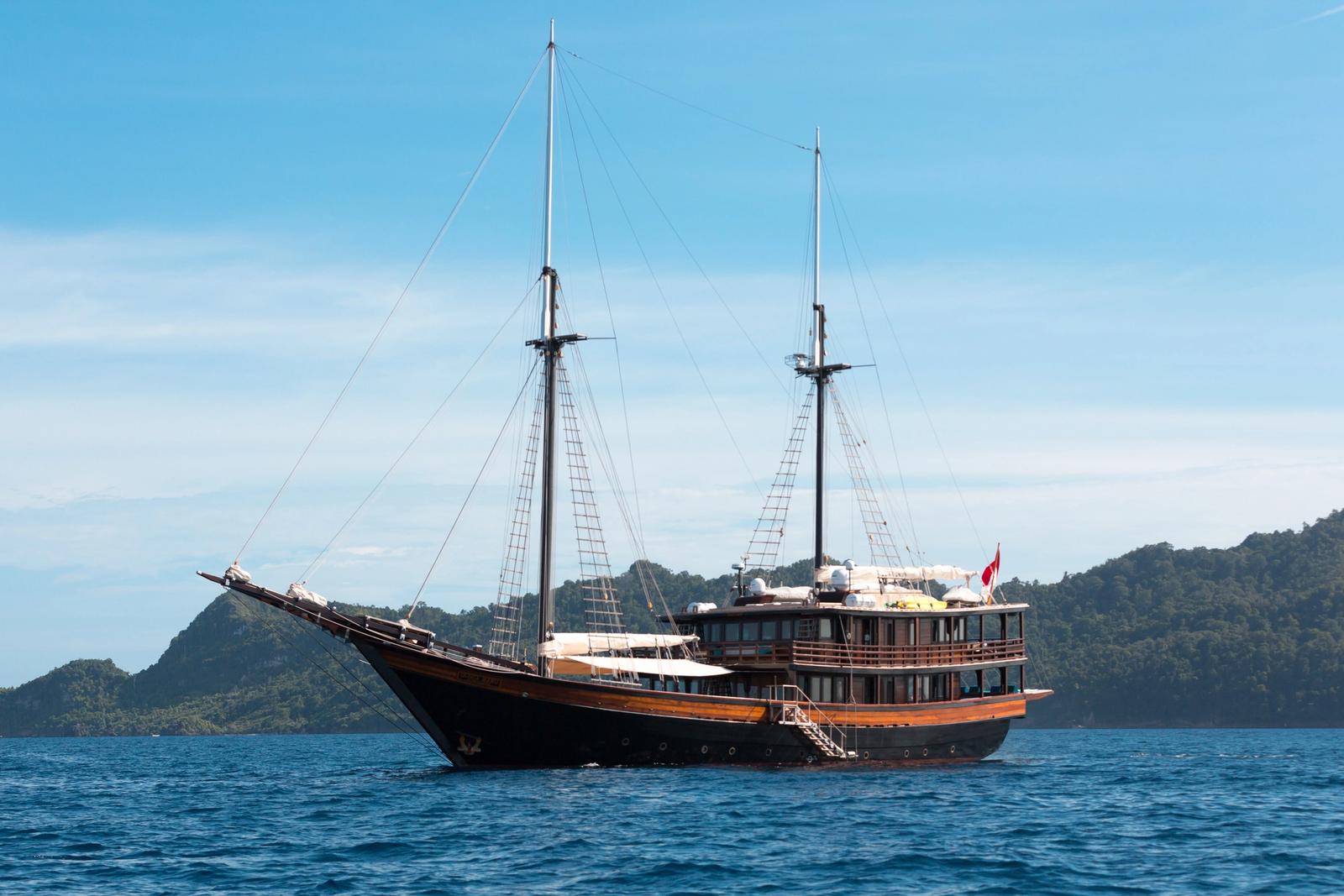 The phinisi Dunia Baru at anchor with forested hills behind
