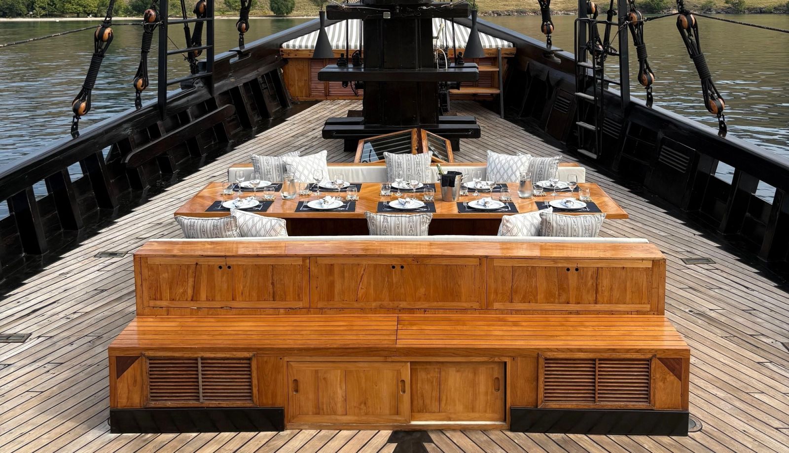 The dining table at the bow of El Aleph set with plates and a wooden bench in front.