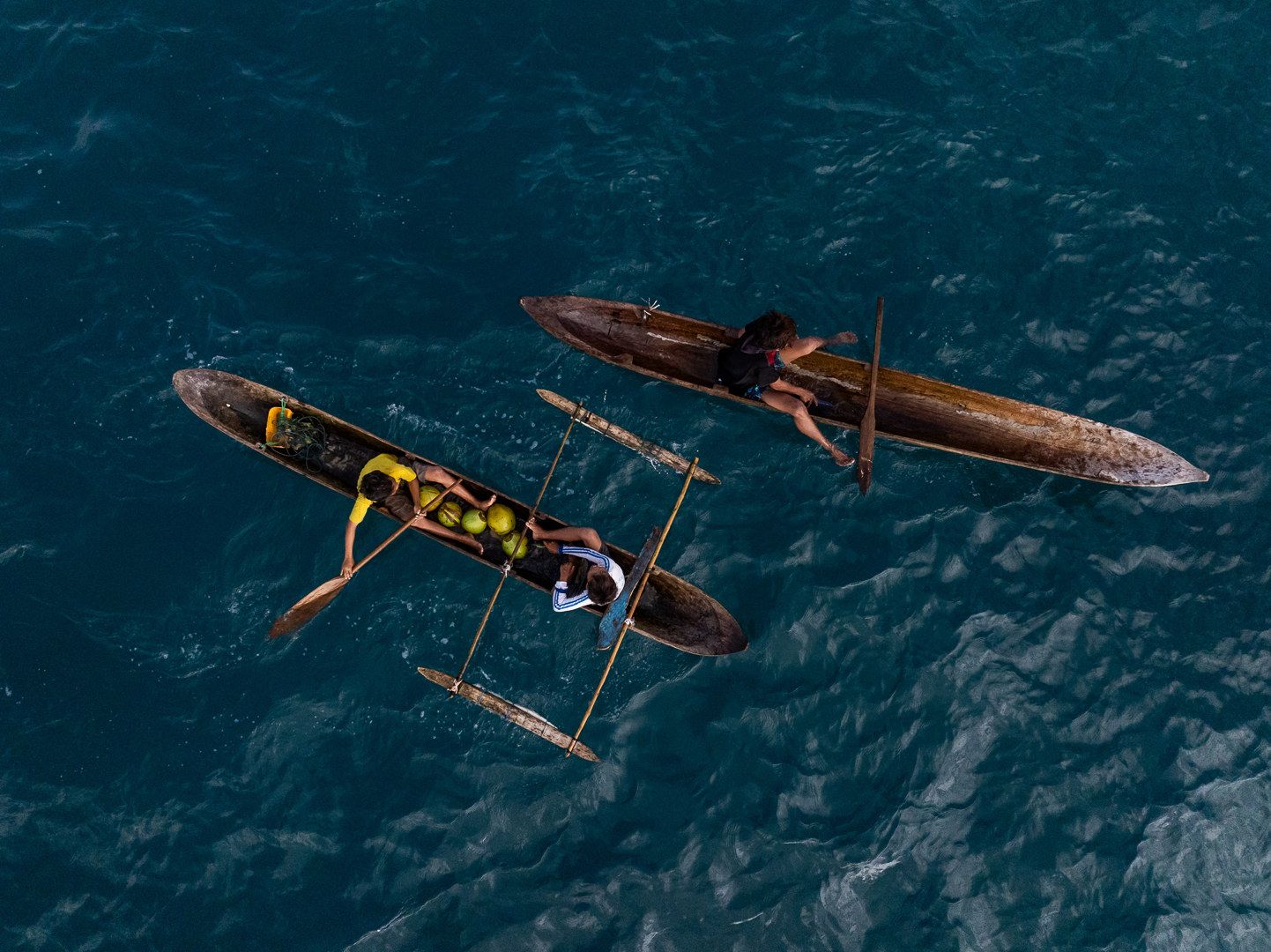 An aerial view of two outrigger canoes on deep blue water.
