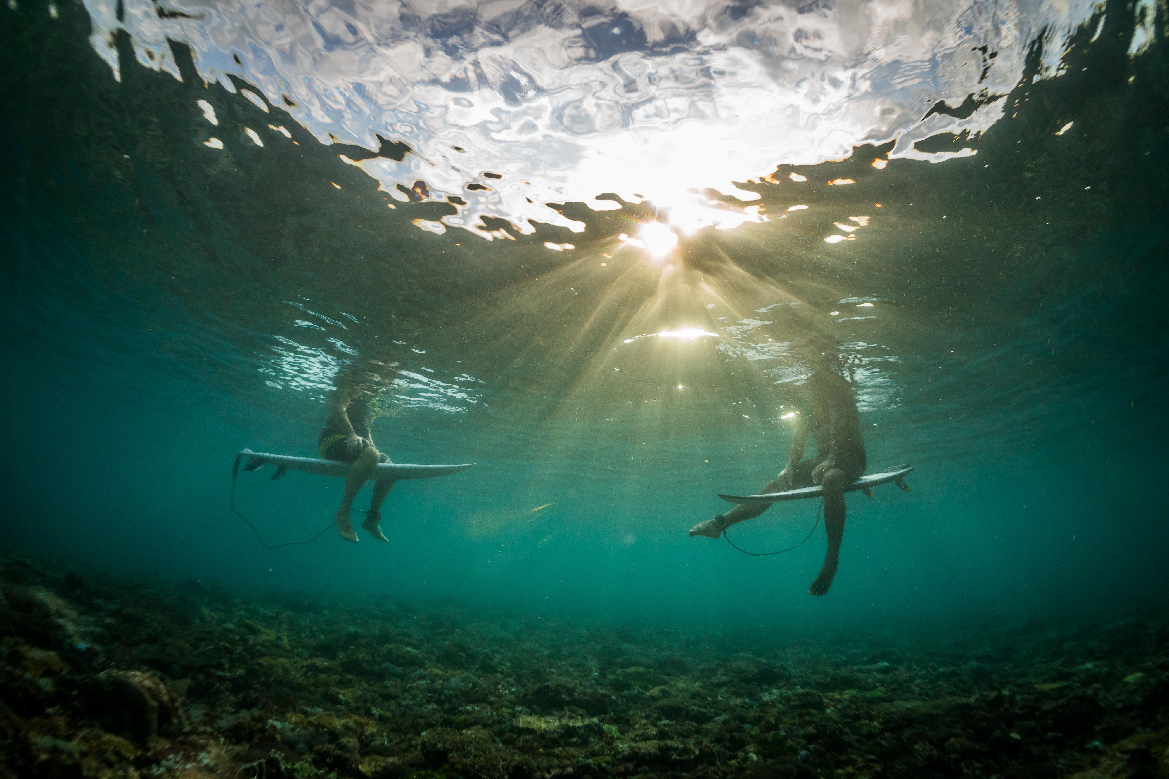 Two surfers sit on their boards at sunset in Indonesian waters