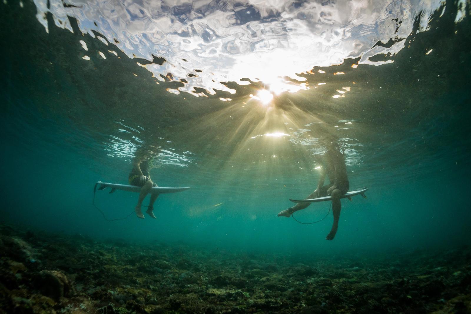 Two surfers sit on their boards at sunset in Indonesian waters