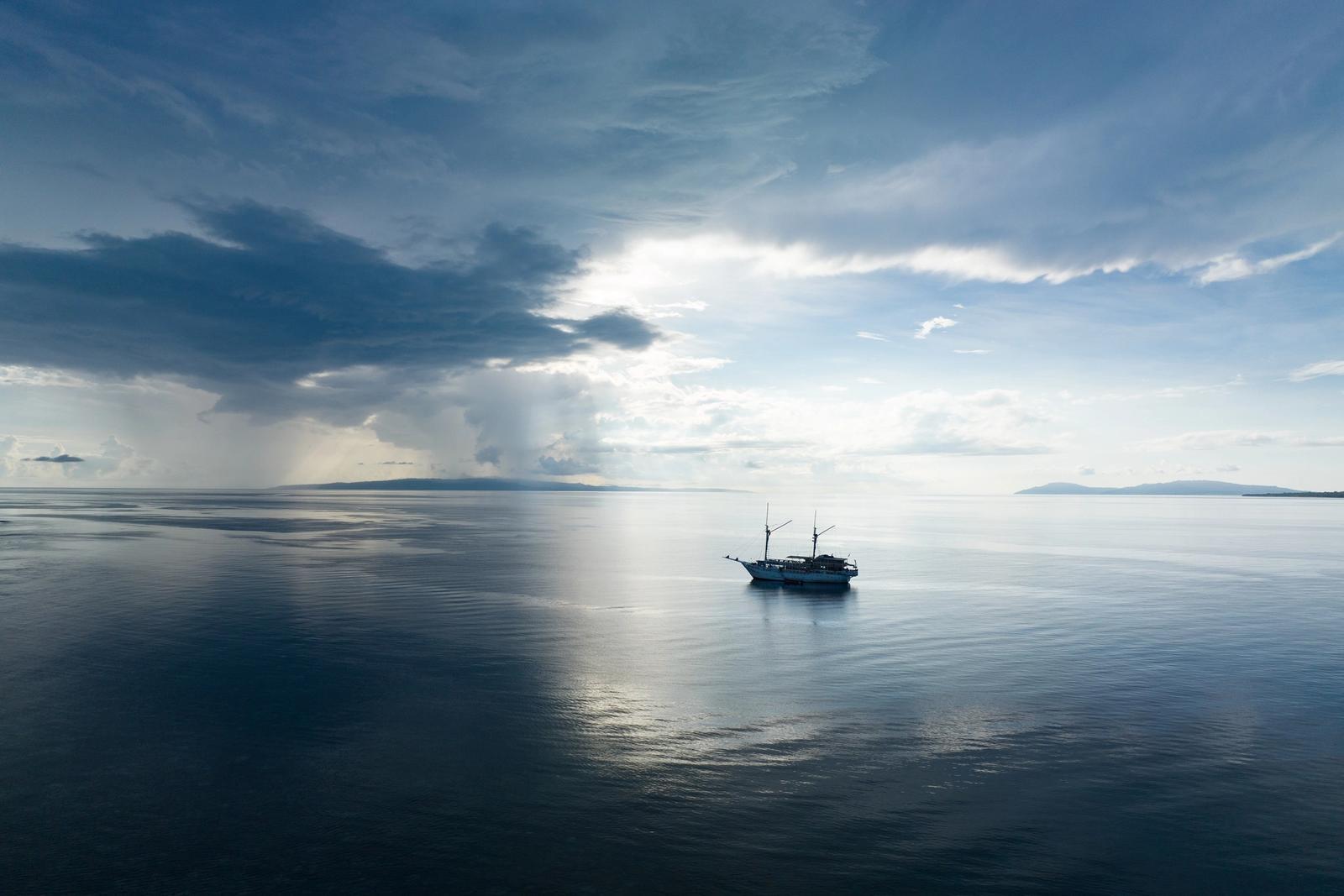 Rain clouds drift across calm seas at sunrise near a remote island in Indonesia. This beautiful area, popular for diving and snorkeling, harbors extraordinary marine biodiversity.