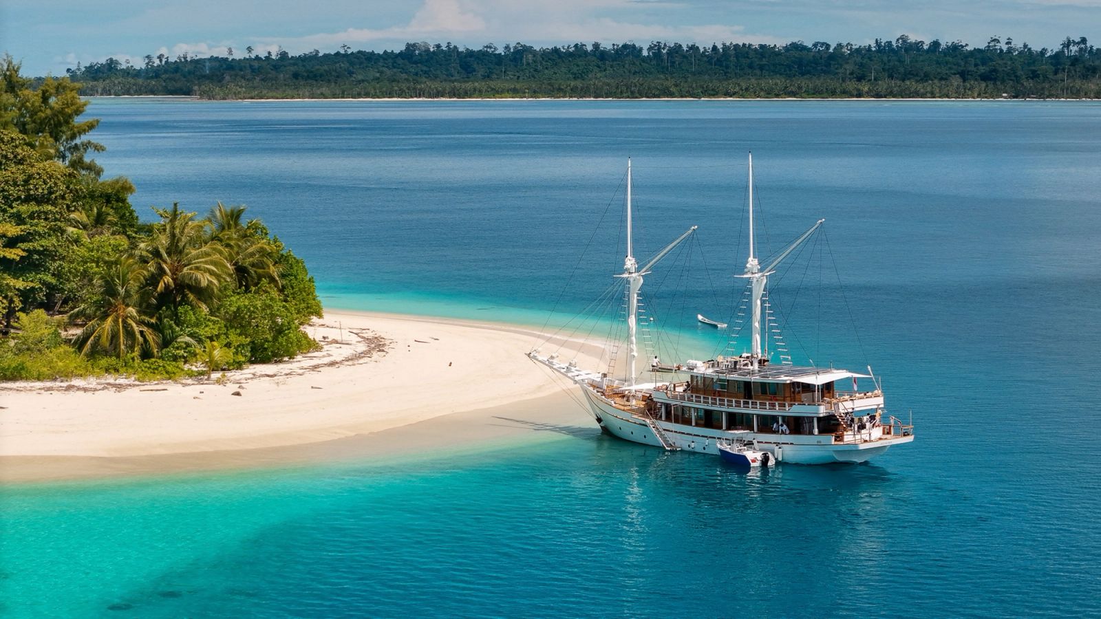 Siloina at anchor off a white sand spit with palm trees and turquoise water.