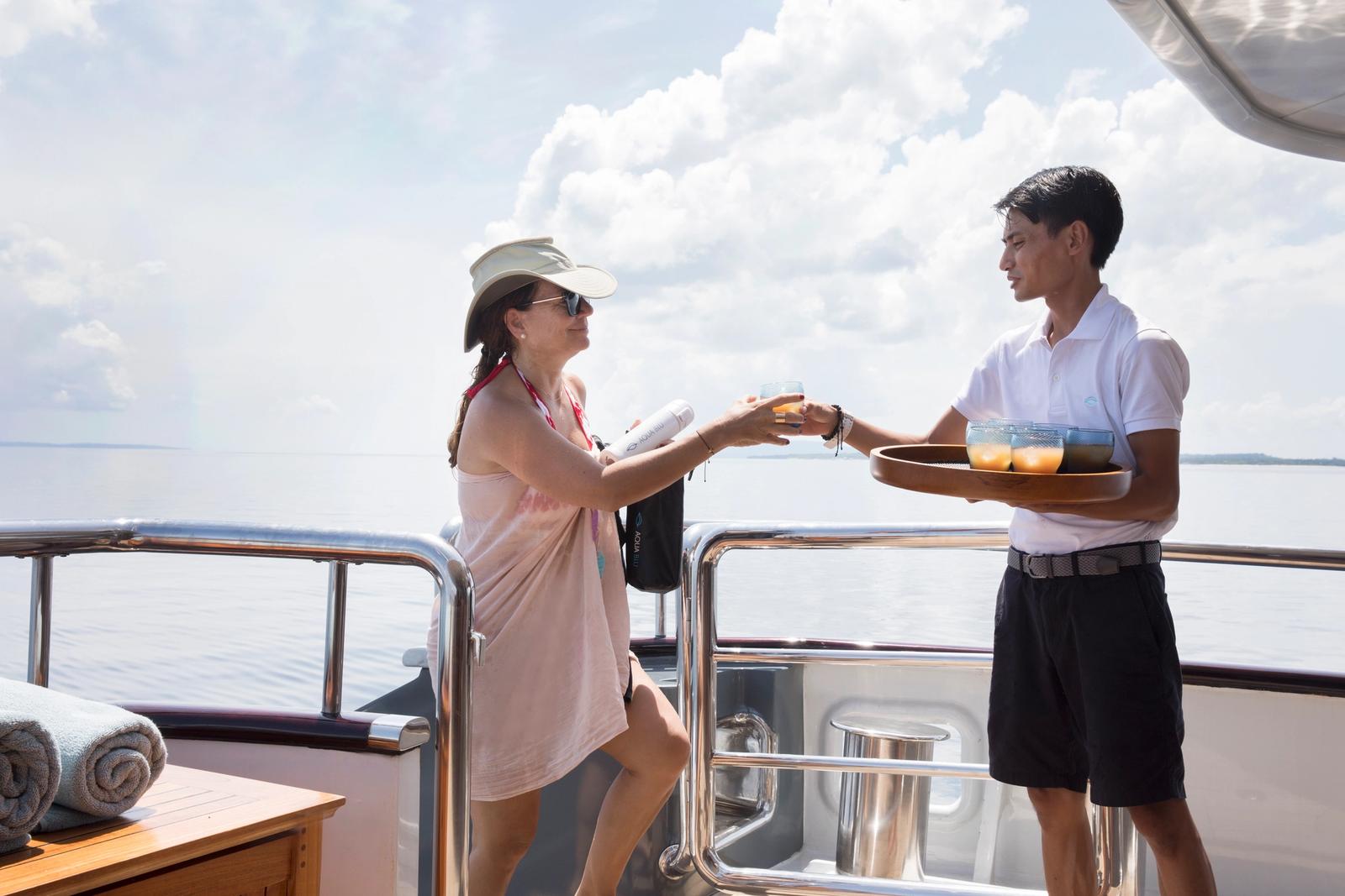 A crew member offers a welcome drink from a tray to a guest on the yacht's deck.