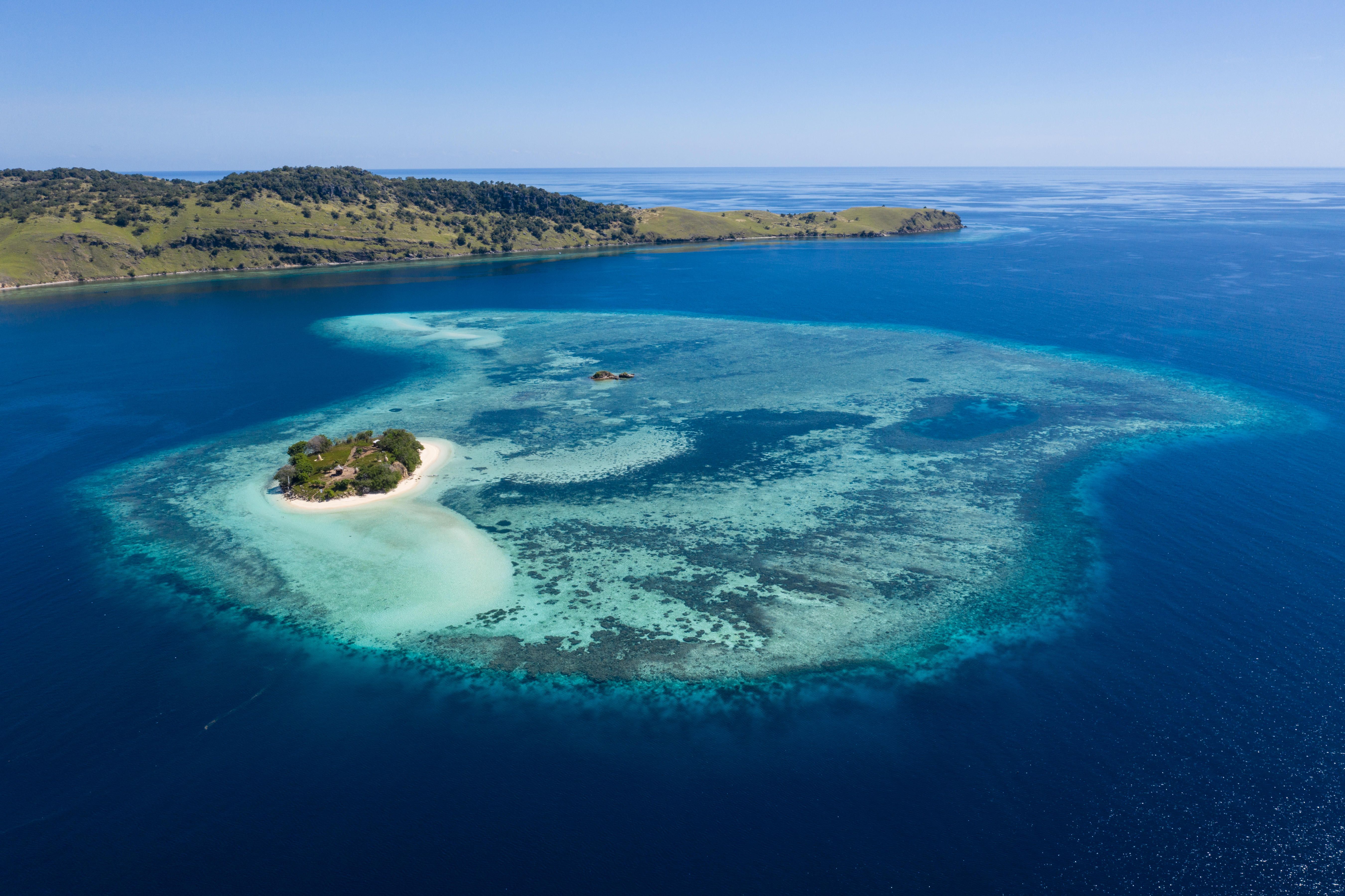A small island and its reef in deep blue water, seen from the air