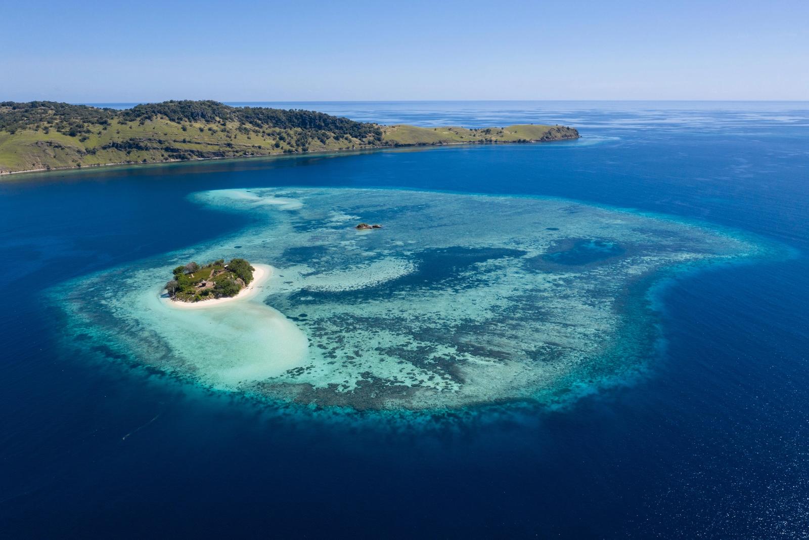 A small island and its reef in deep blue water, seen from the air