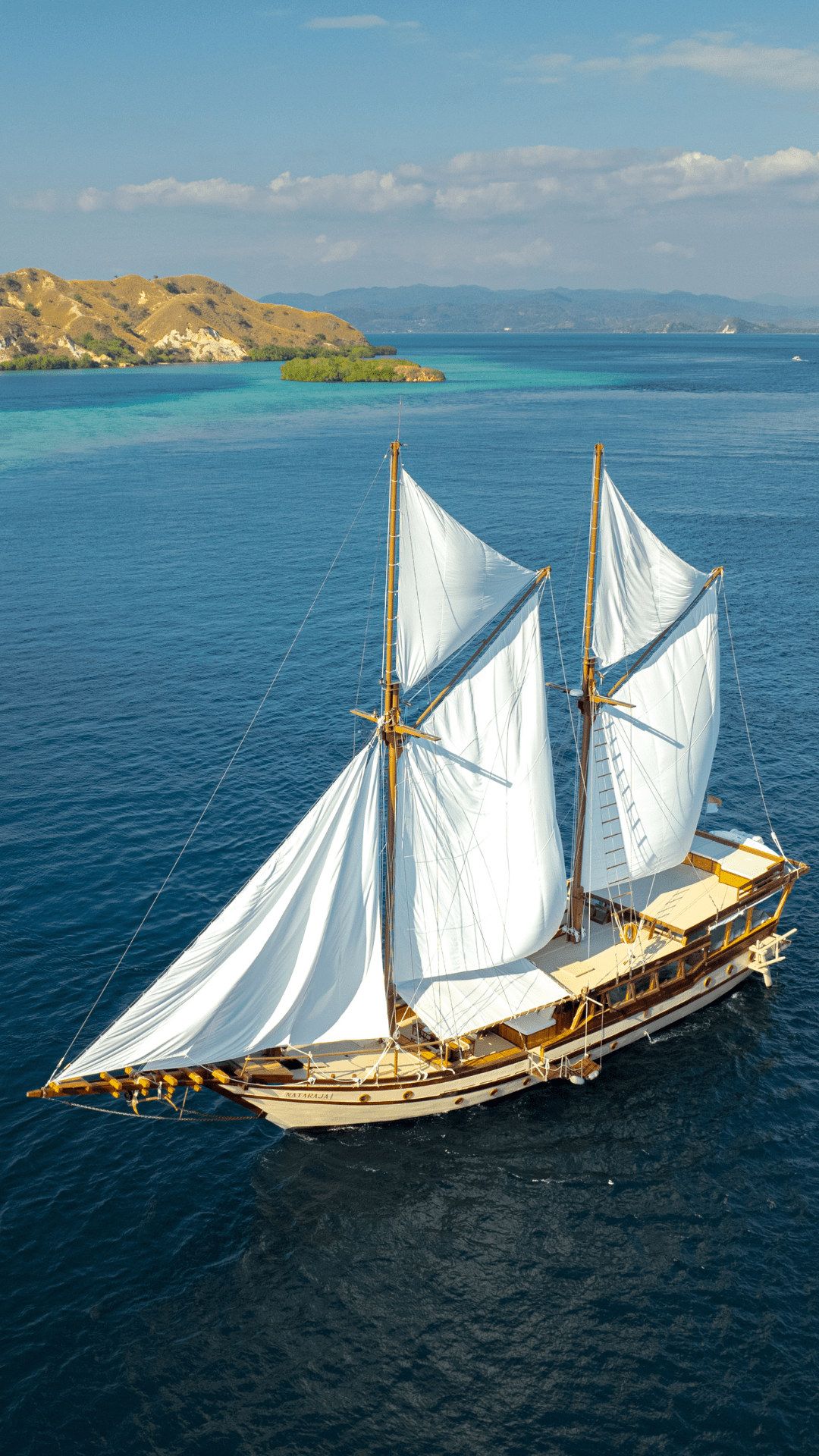 A phinisi under sail off the coast, seen from above.