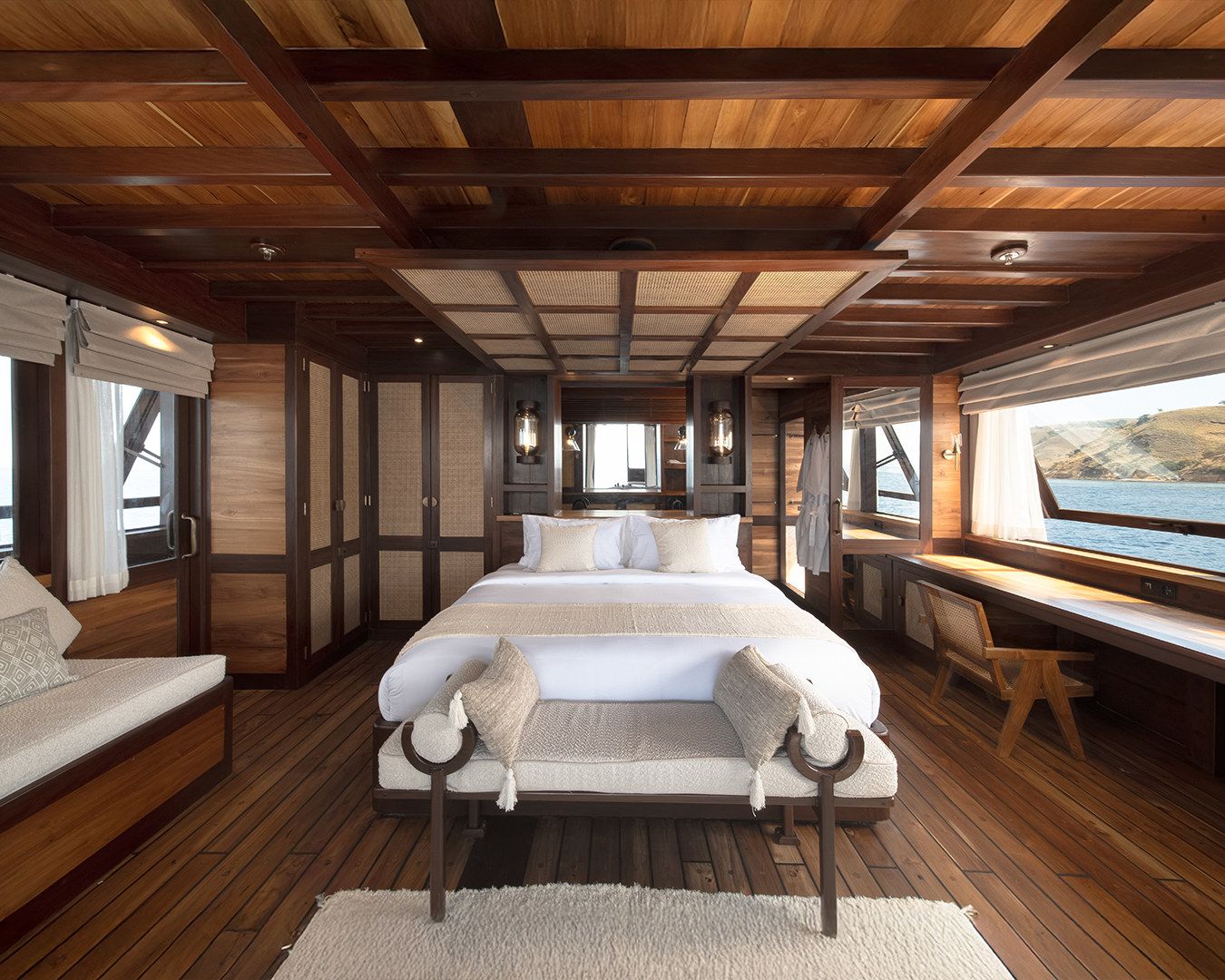 A wide cabin on Sanya with a double bed, a bench at its foot and a desk beneath the windows.