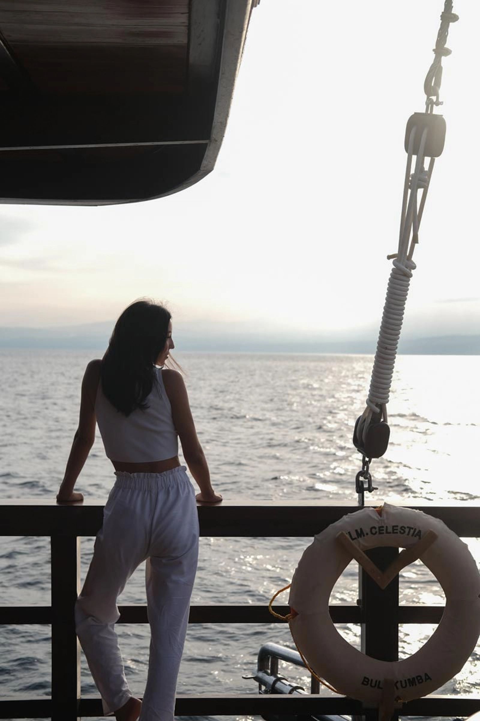 A woman standing at the rail of Celestia beside a life ring looking at the sea.