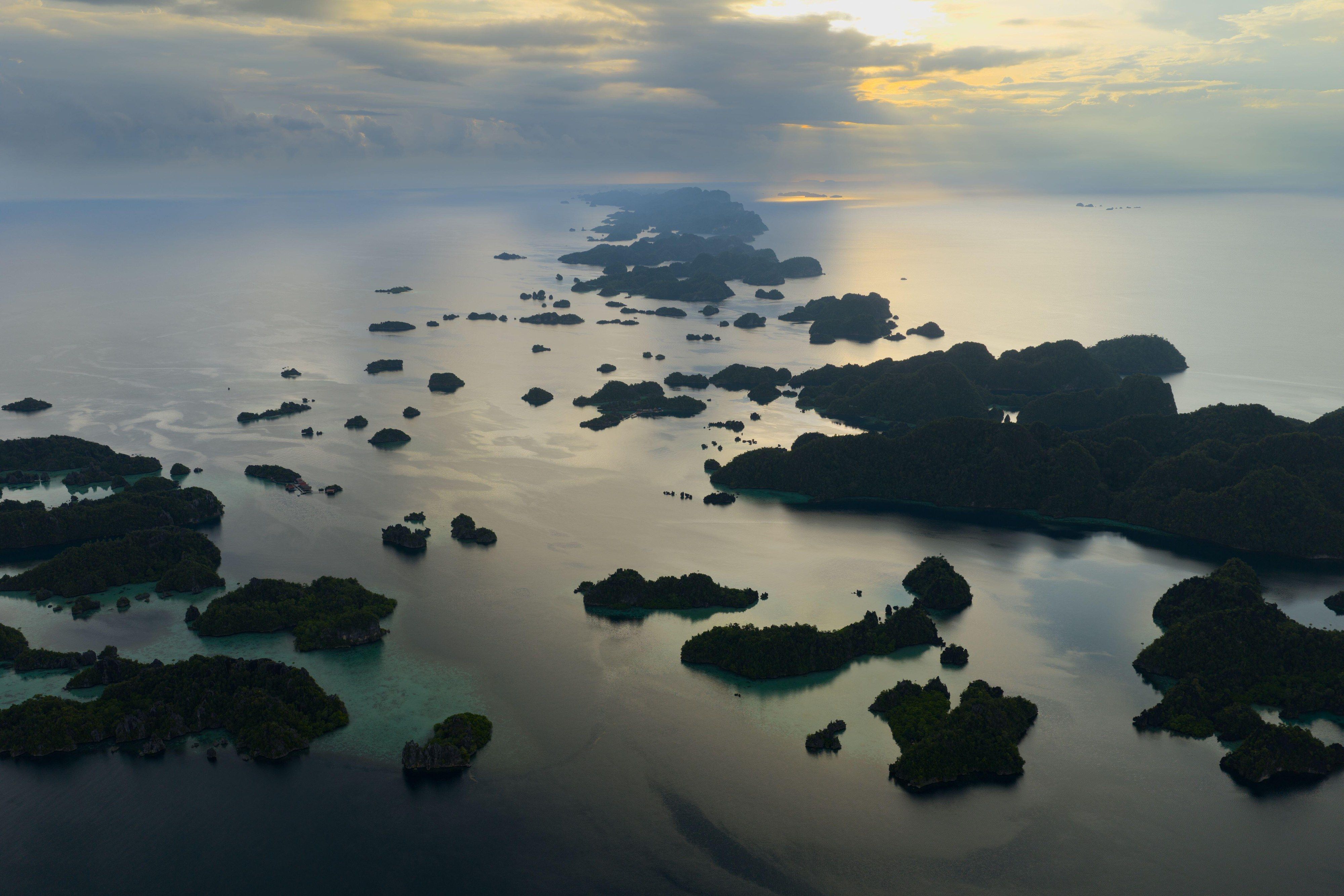 A serene sunrise illuminates scenic limestone islands in Misool, Raja Ampat.