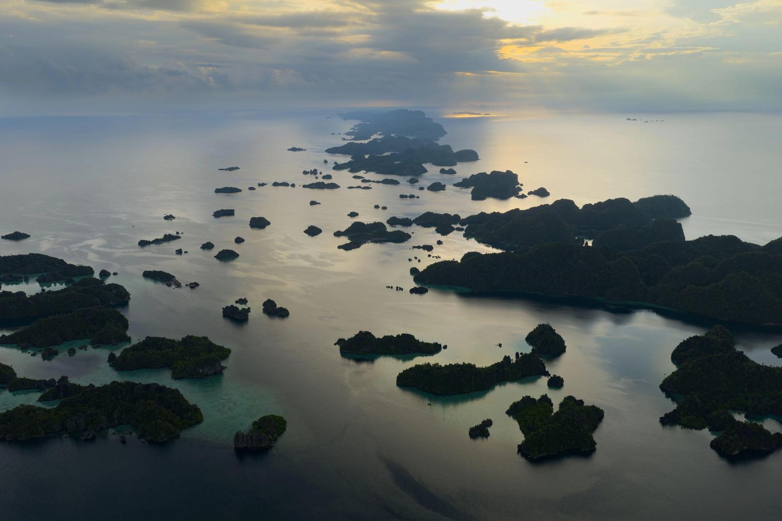 A serene sunrise illuminates scenic limestone islands in Misool, Raja Ampat.