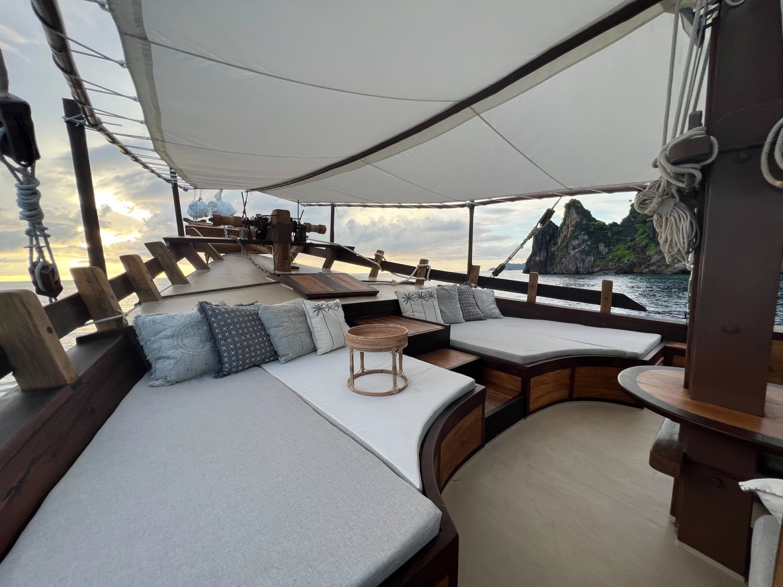 A cushioned daybed and bench seating on the foredeck of Dewata at sunrise.