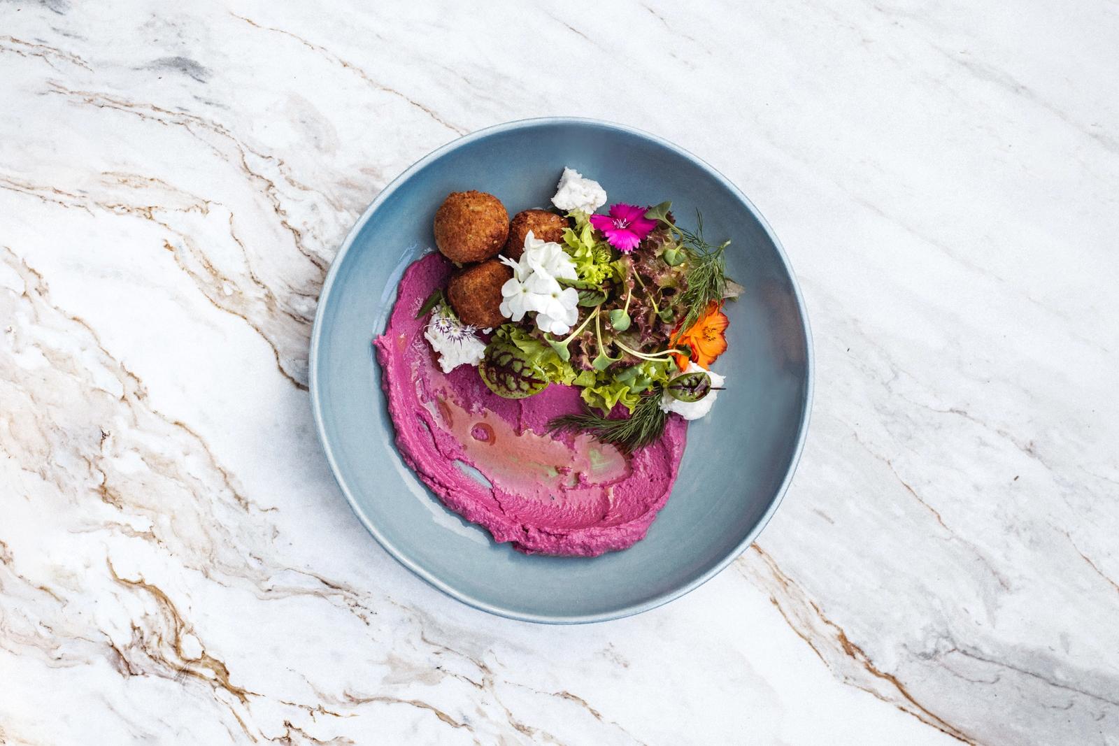 A plated dish of falafel, greens and beet puree on a marble table